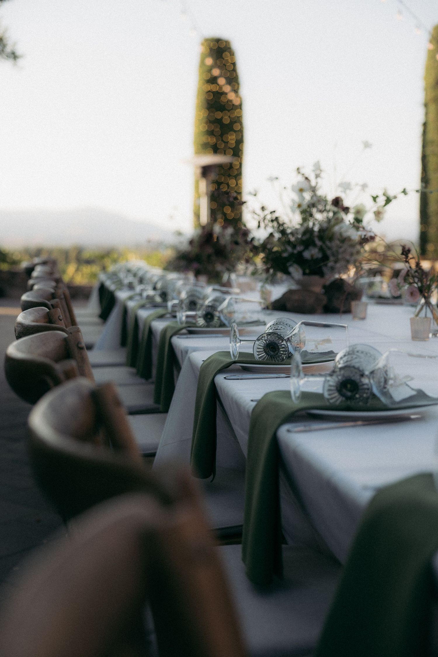 Elegant wedding reception table setting with green chairs and floral centerpieces overlooking a scenic view.