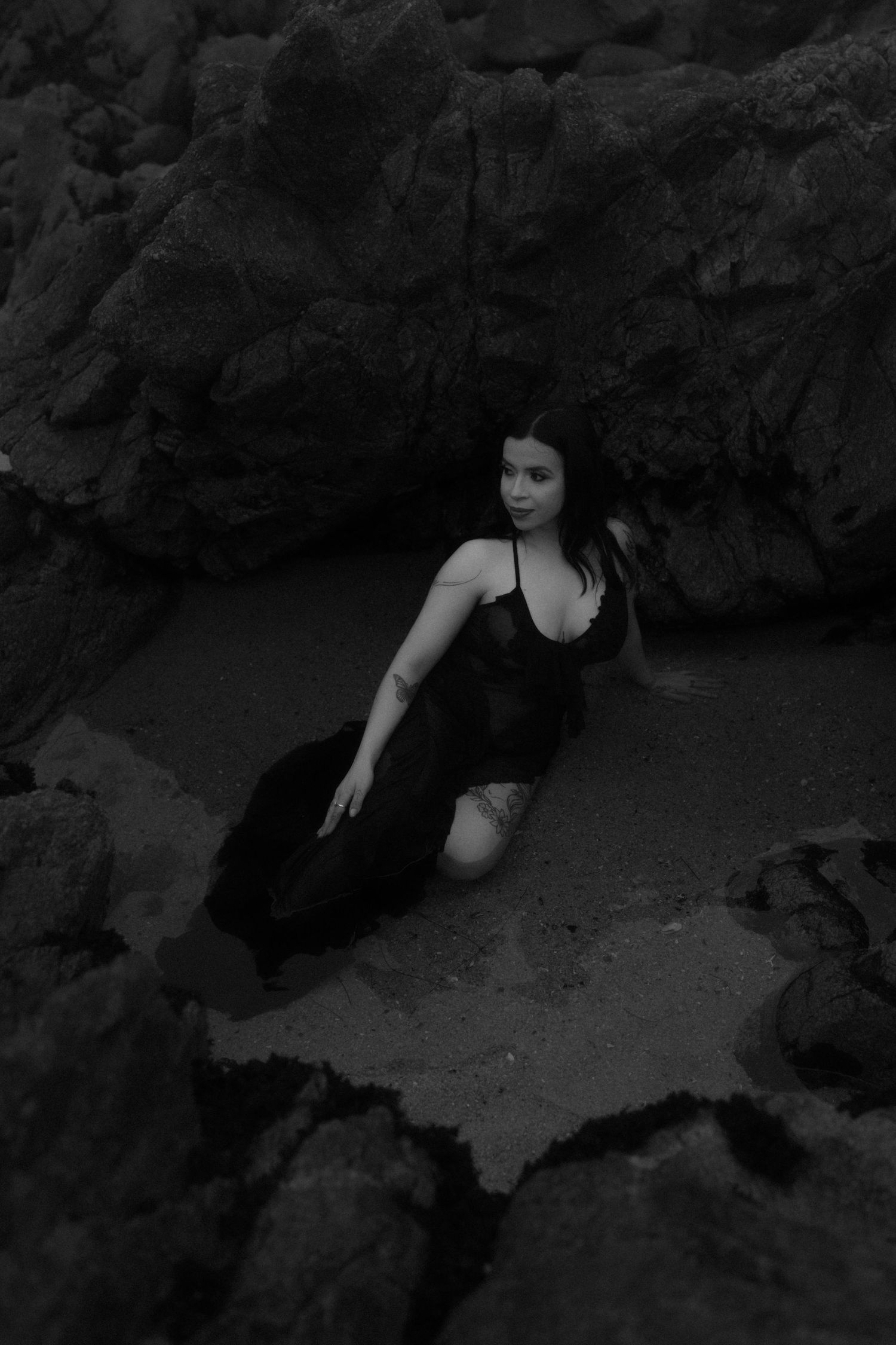 A person in dark clothing emerges from a shadowy rocky cave entrance in a dramatic black and white photograph.