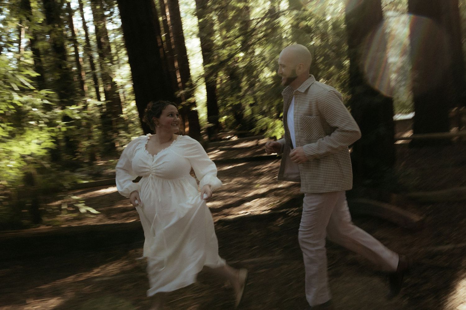 Two people in light colored clothing practice martial arts moves together in a sunlit forest setting.