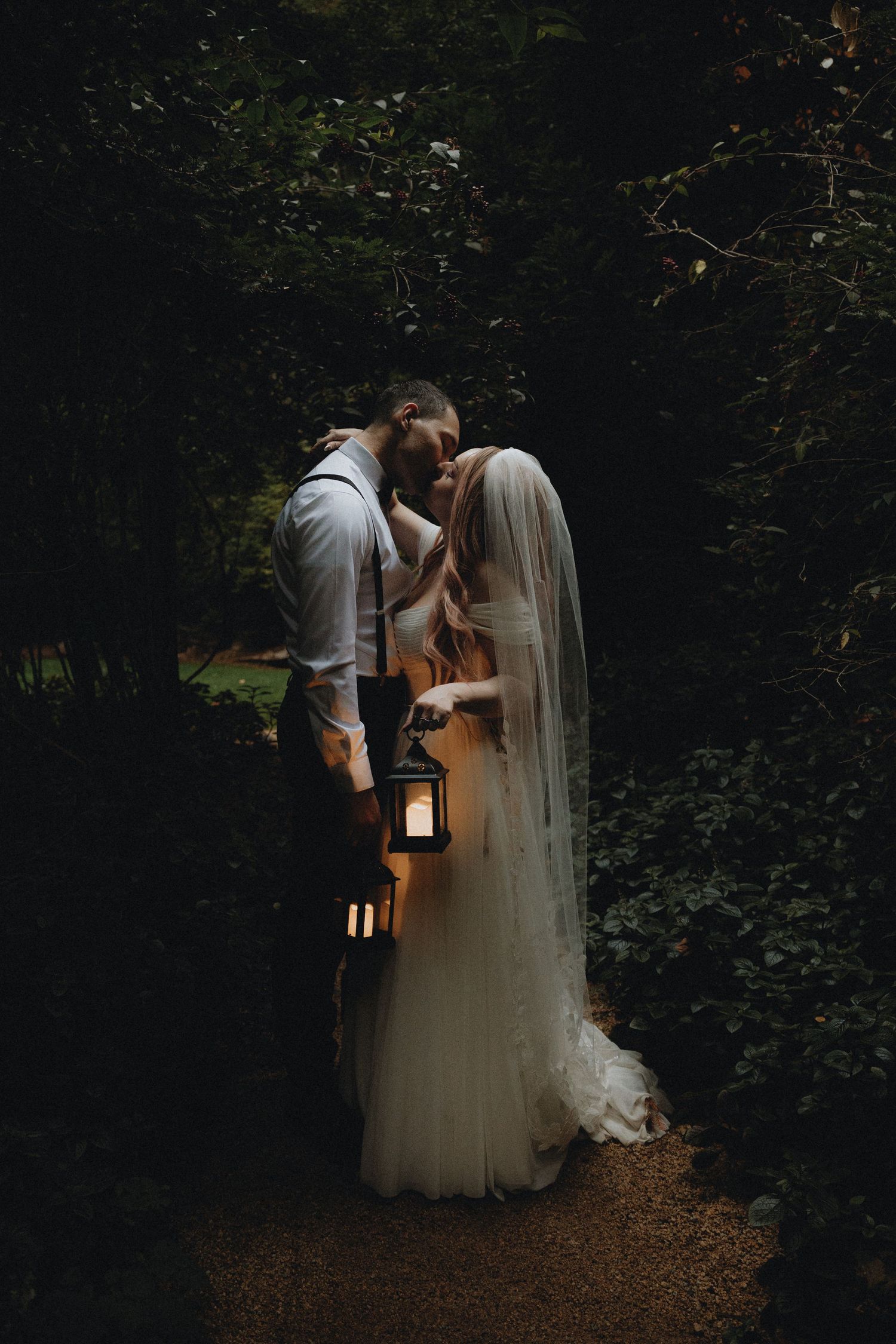 A romantic moment captured in a dark forest setting with a glowing lantern casting warm light.
