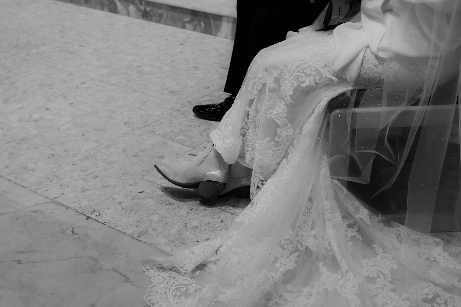 A close-up view of a bride's white wedding dress train and veil trailing on the ground.