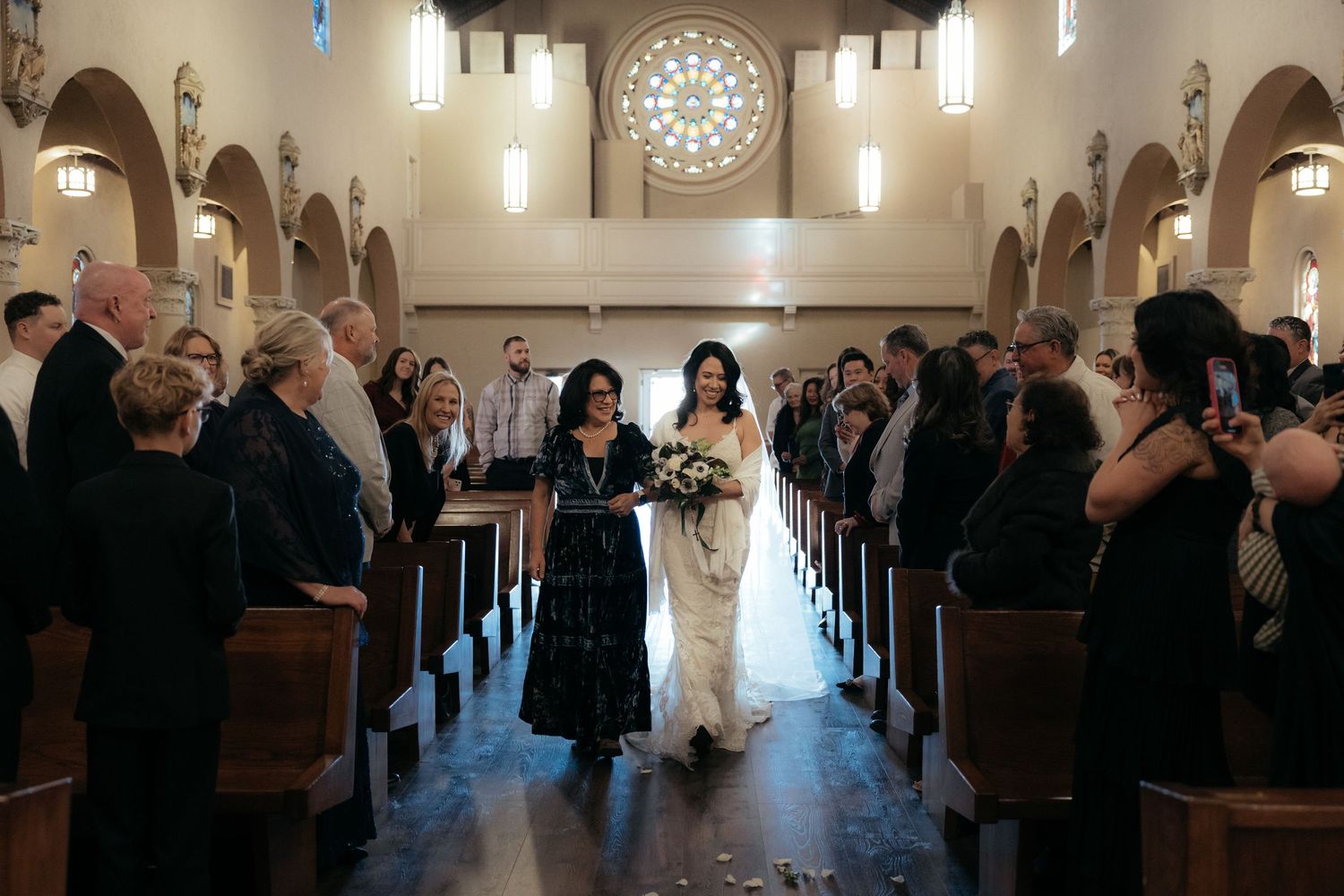 Wedding guests stand and raise their hands in celebration during a church ceremony.