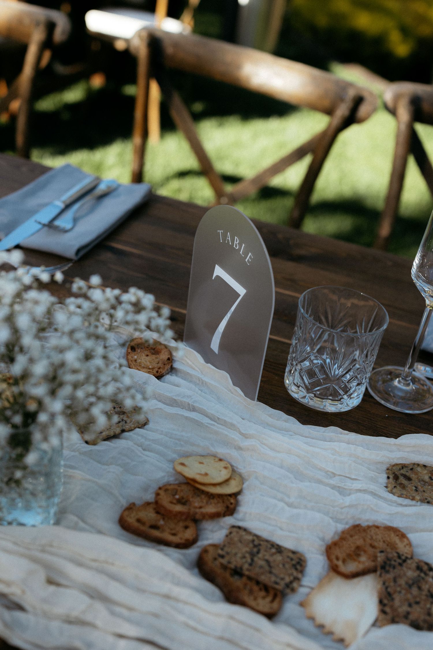 Elegant outdoor wedding reception table 7 with crystal glasses, assorted crackers, baby's breath florals, and linen runner.