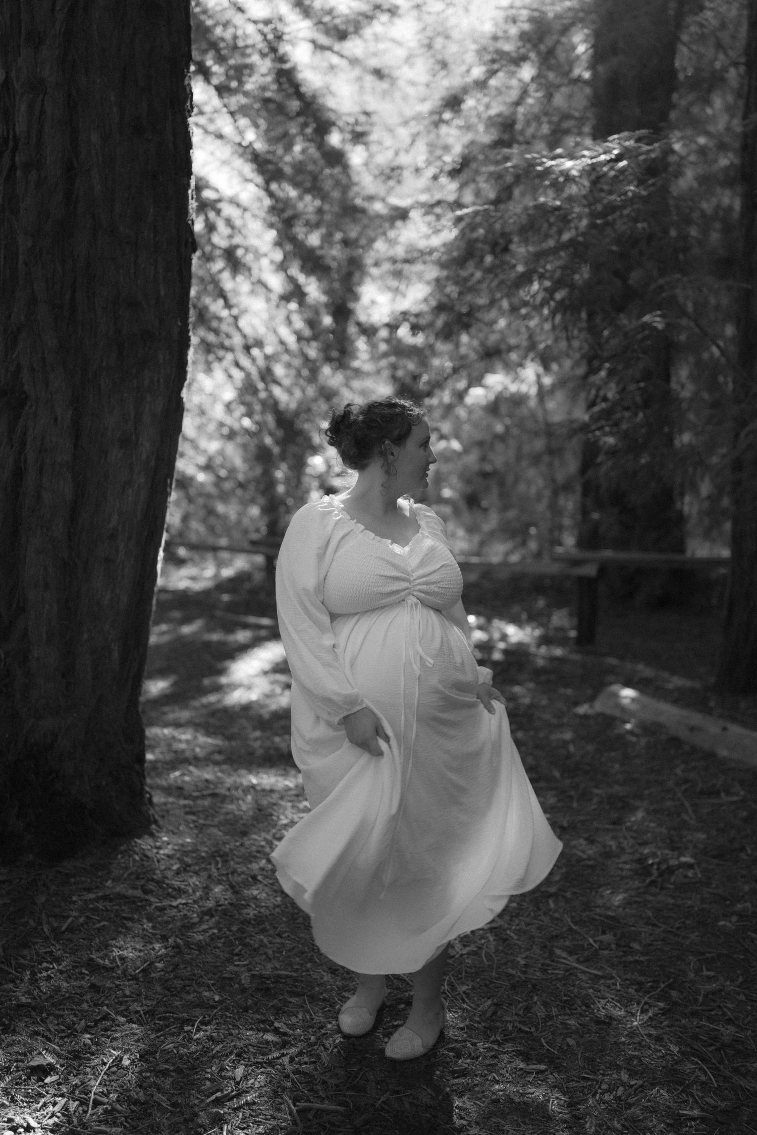 Woman in white dress twirling in black and white forest photography.