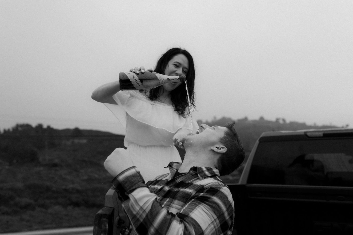 Couple lounging together in truck bed against misty coastal backdrop.