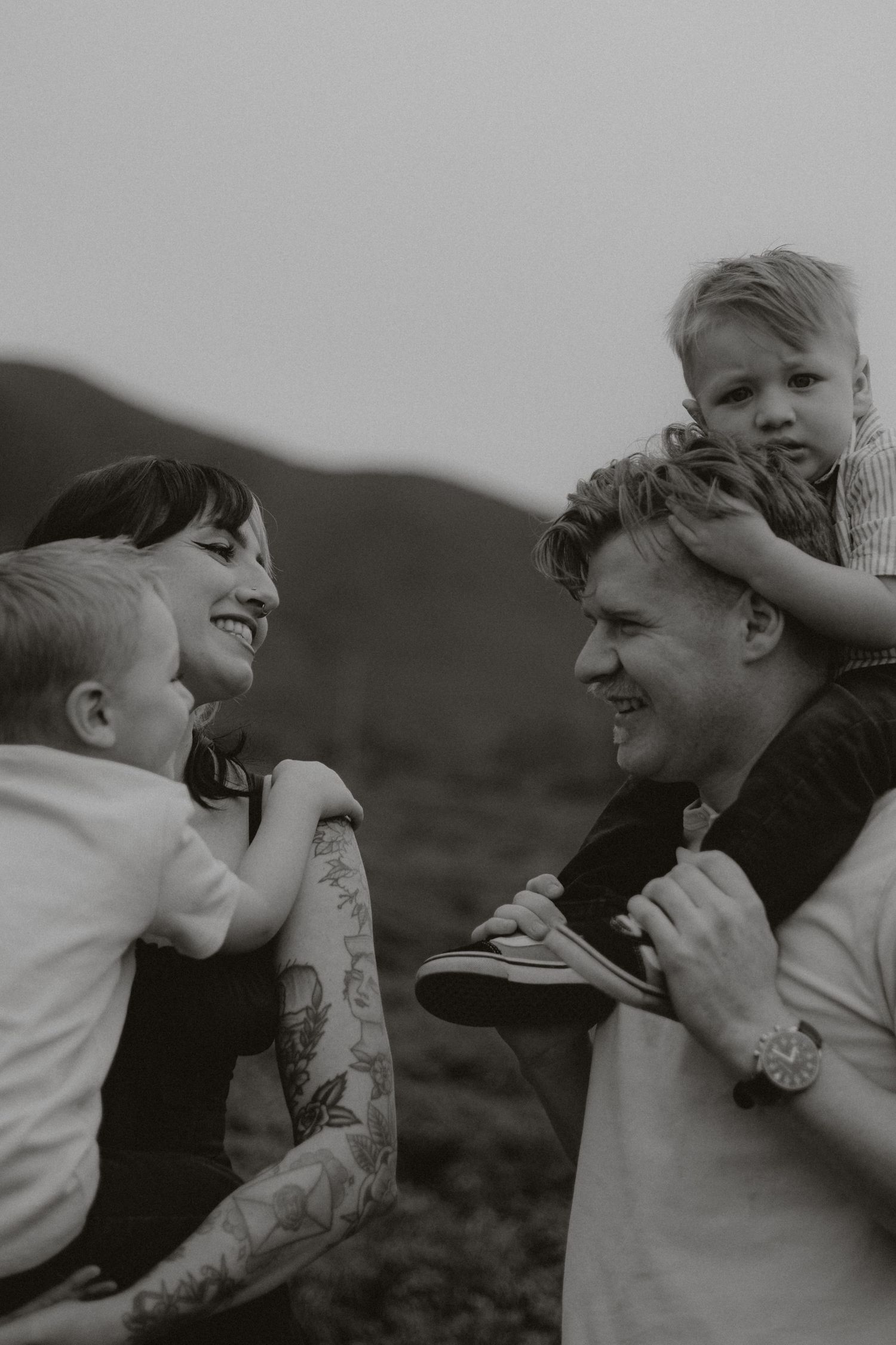 Black and white photo of a happy family with two young boys outdoors in a scenic mountain setting.