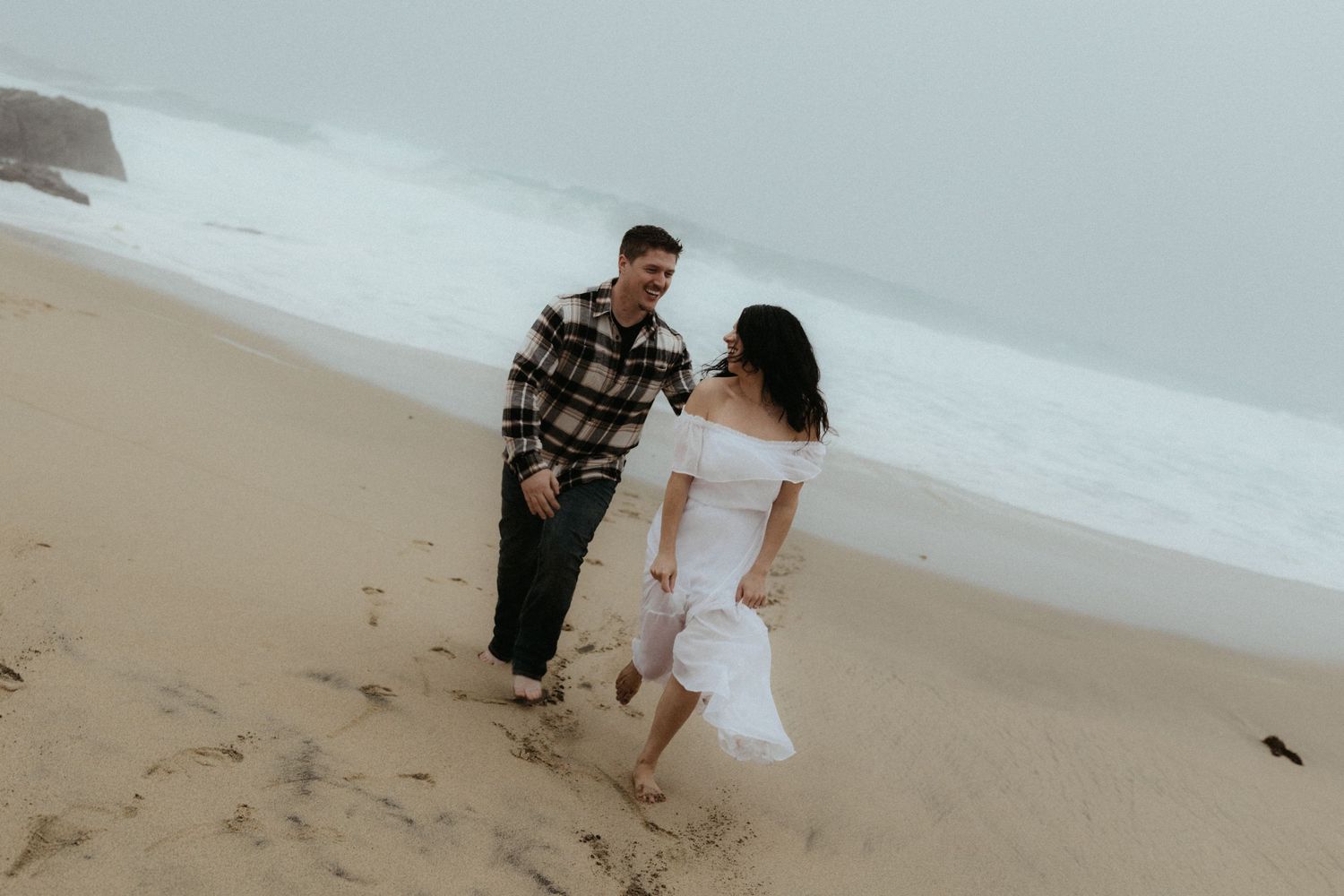 A couple shares a romantic moment on a sandy beach during an overcast day.
