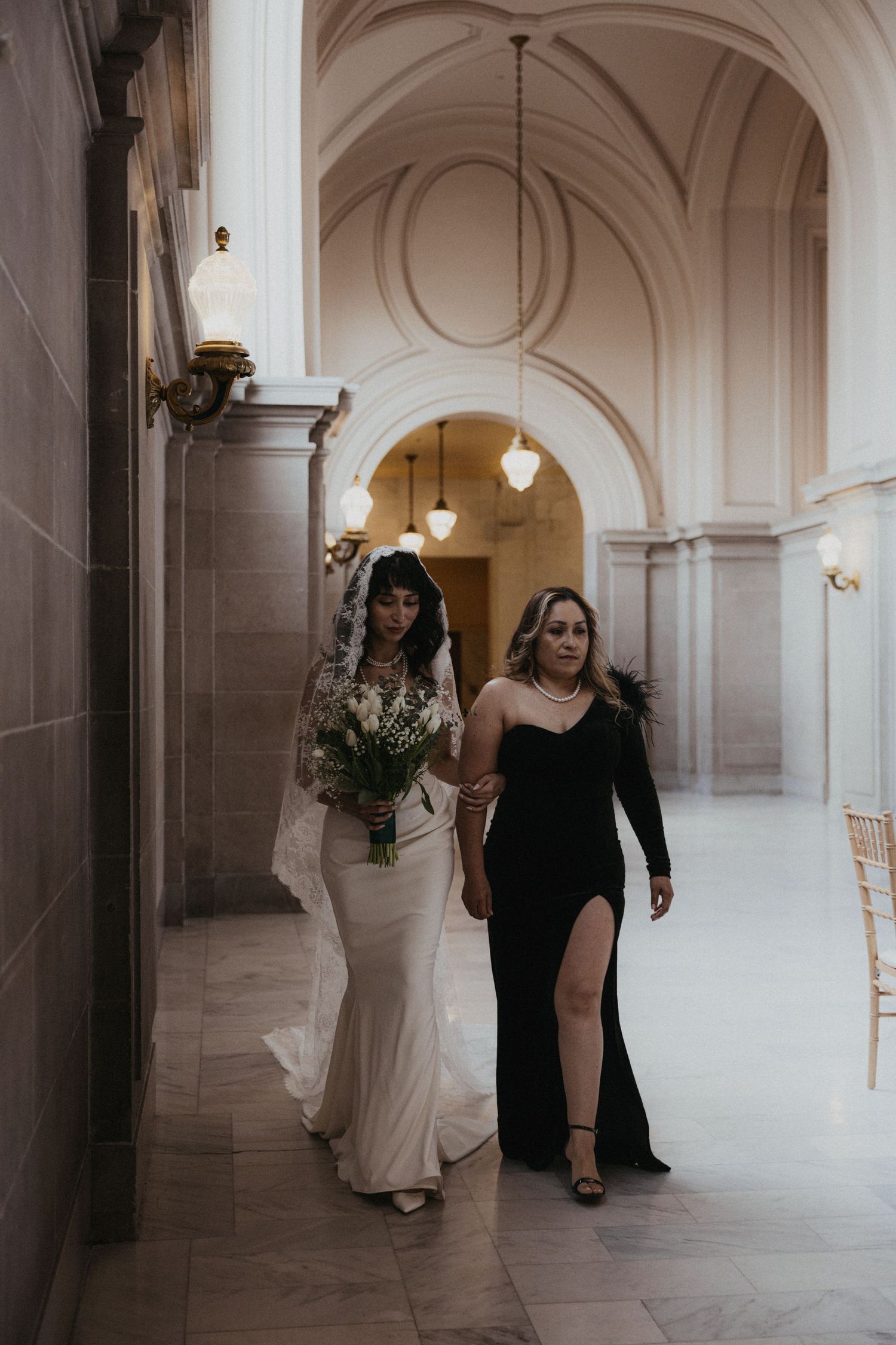 Bridal party members walking down a bright white corridor with classical architectural details.