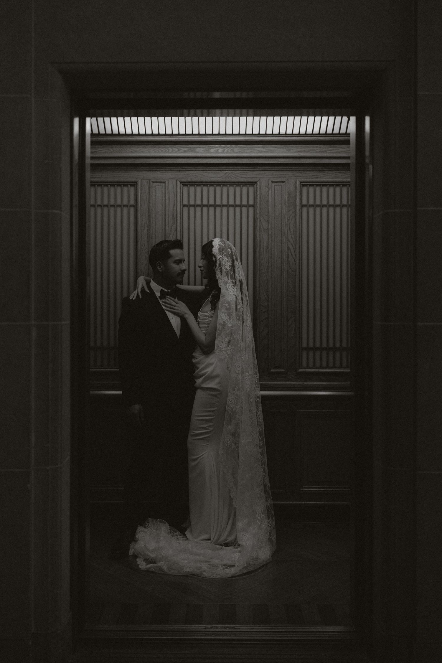 A moody wedding portrait of a couple framed within an elegant doorway.