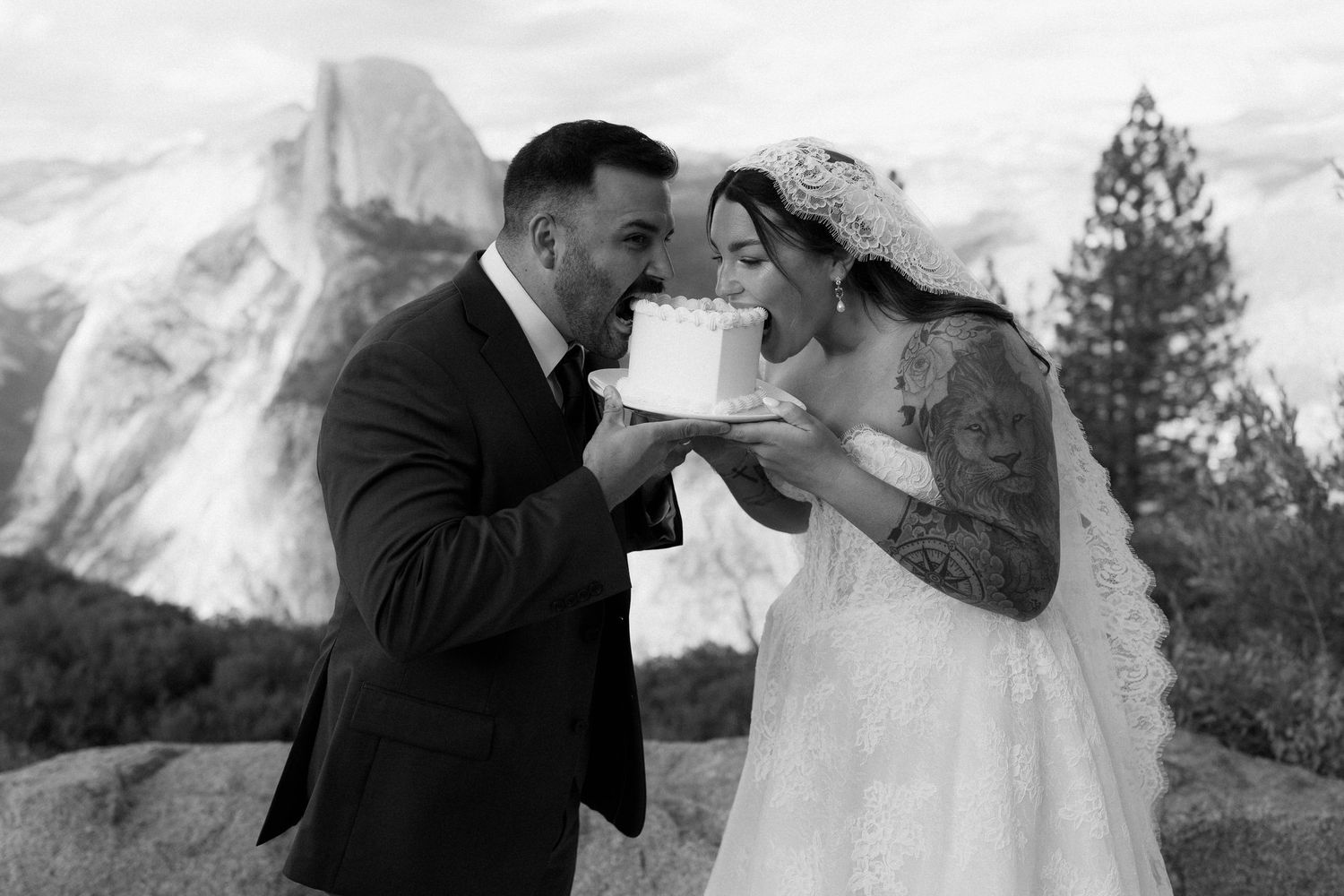 Bride and groom sharing a bite of wedding cake with Half Dome Yosemite in black and white background.