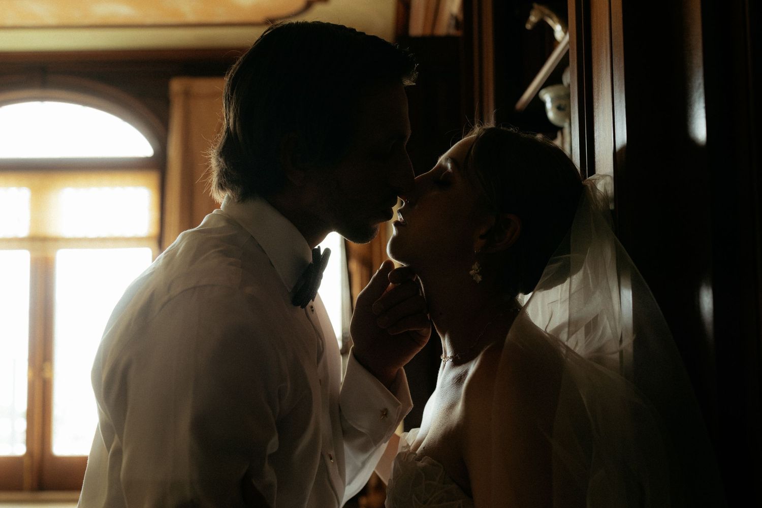 Romantic silhouette of bride and groom almost kissing in warmly lit vintage interior setting.