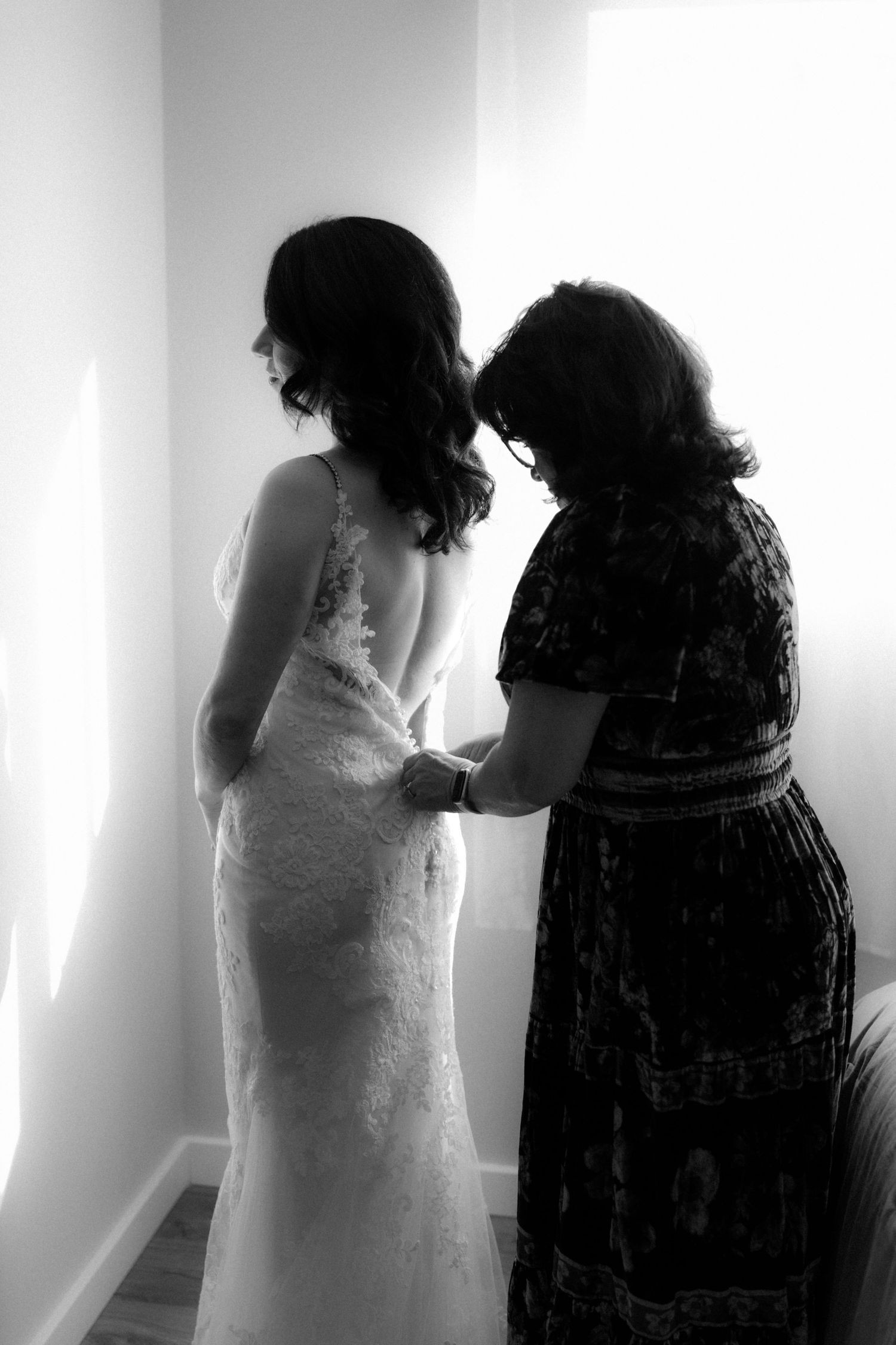 Black and white photo of two women in formal dresses standing together in a bright room.