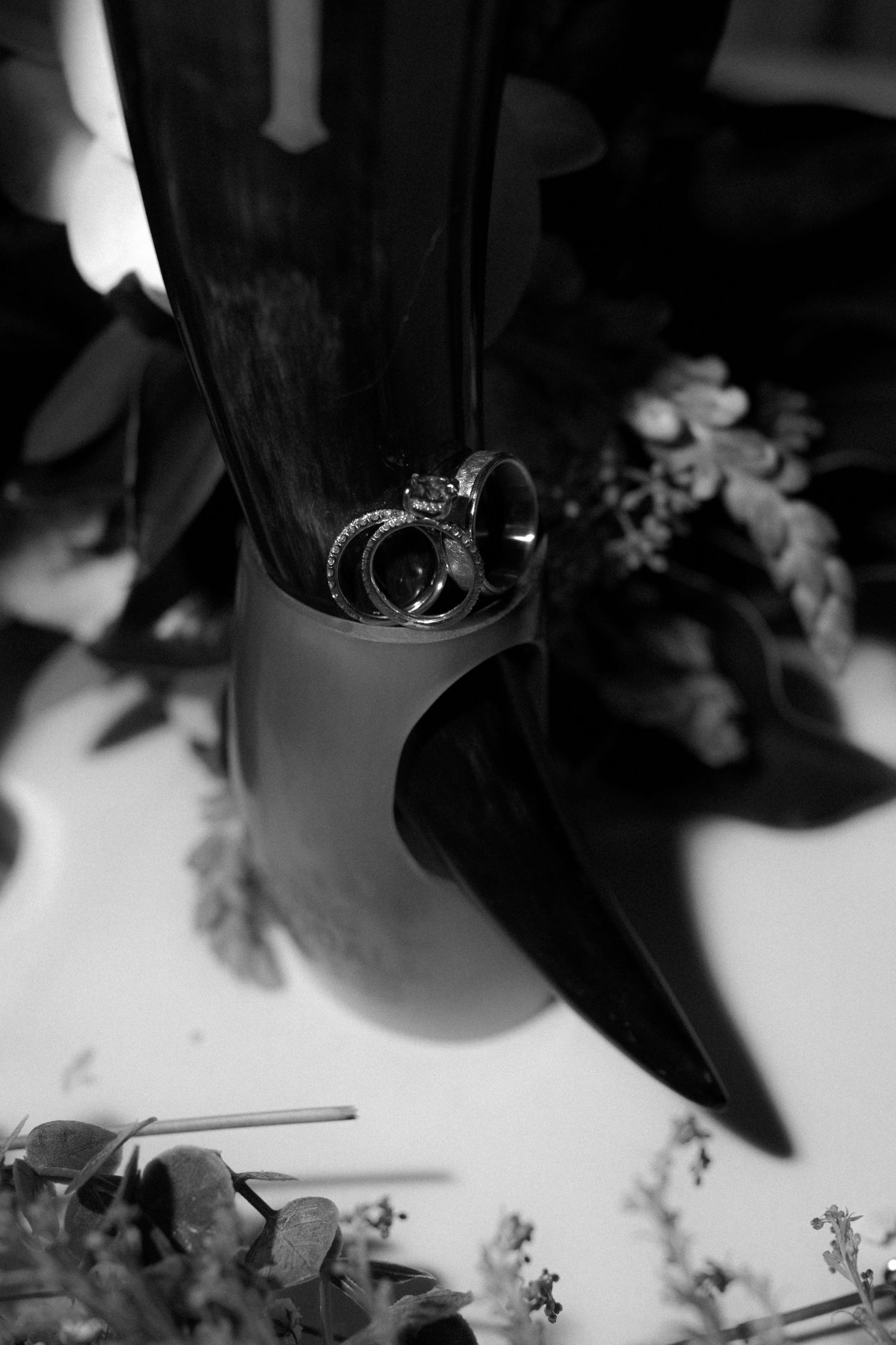 Wedding rings rest elegantly on a black surface surrounded by delicate flowers in a moody black and white composition.
