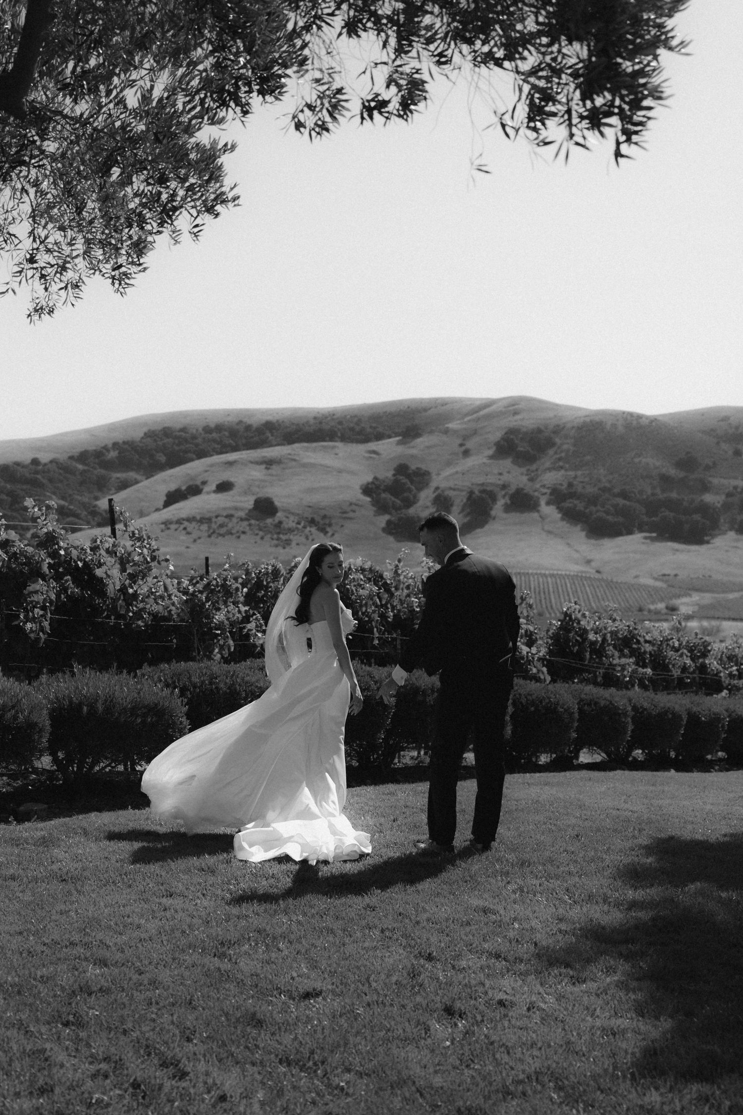 A couple poses for wedding photos on a hillside with rolling landscapes in the background.