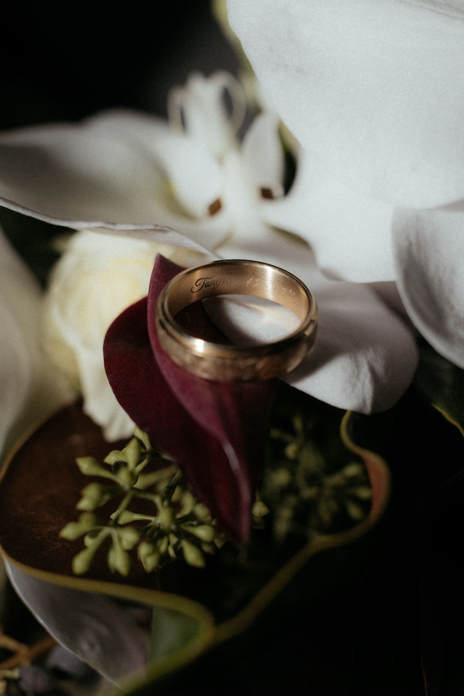 Close-up shot of a gold wedding ring resting on delicate white flower petals.