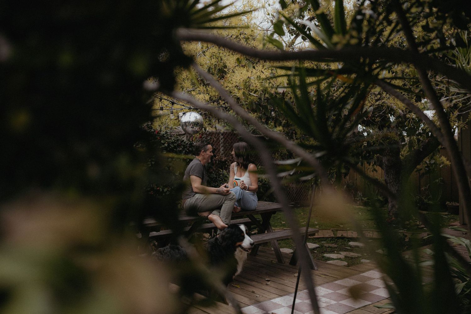 A couple sits together on a bench surrounded by lush greenery in a romantic garden setting.