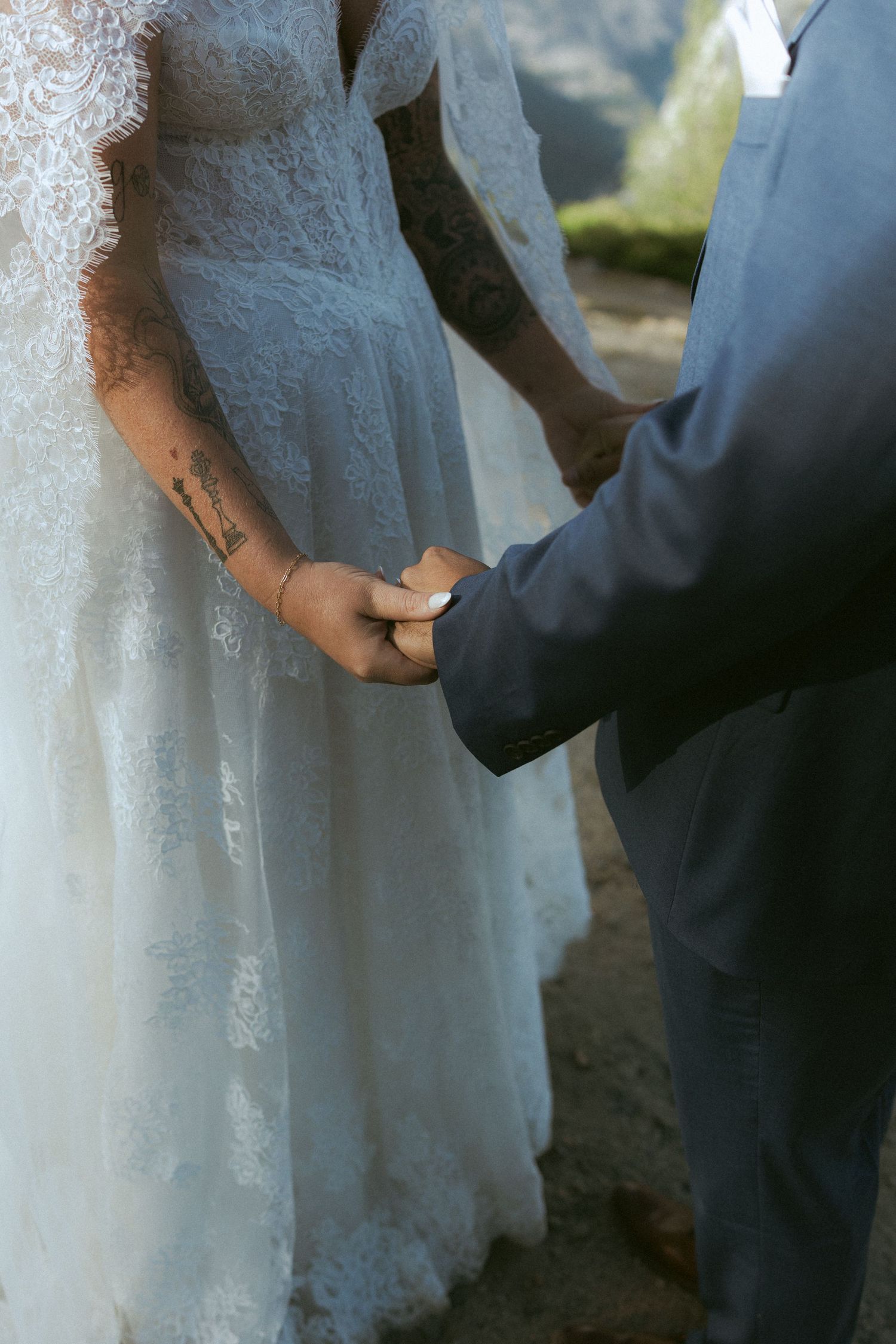 Close-up of tattooed bride and groom holding hands during Yosemite wedding ceremony.