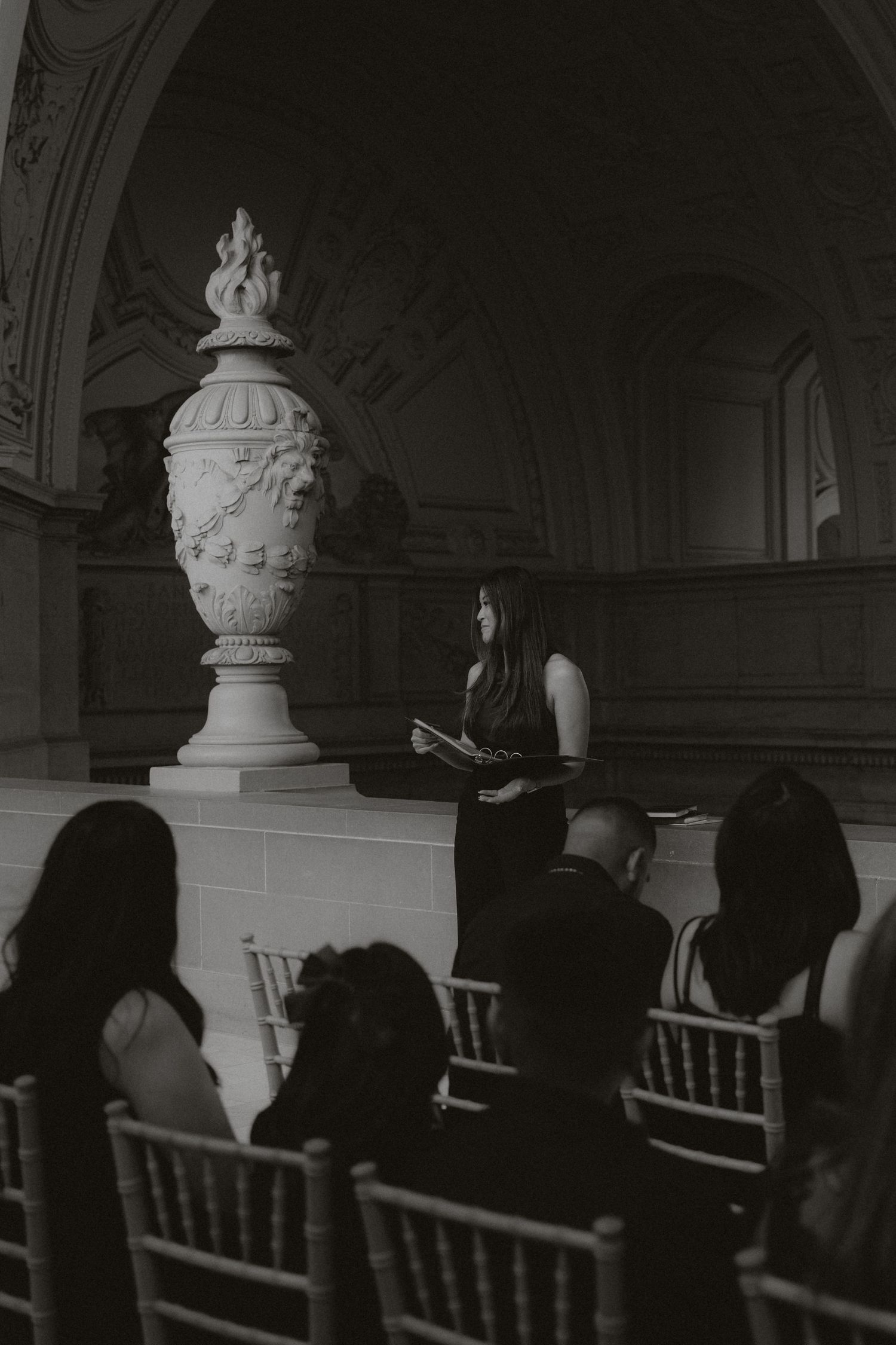 Dark and moody wedding ceremony scene with ornate architectural details and decorative urns.