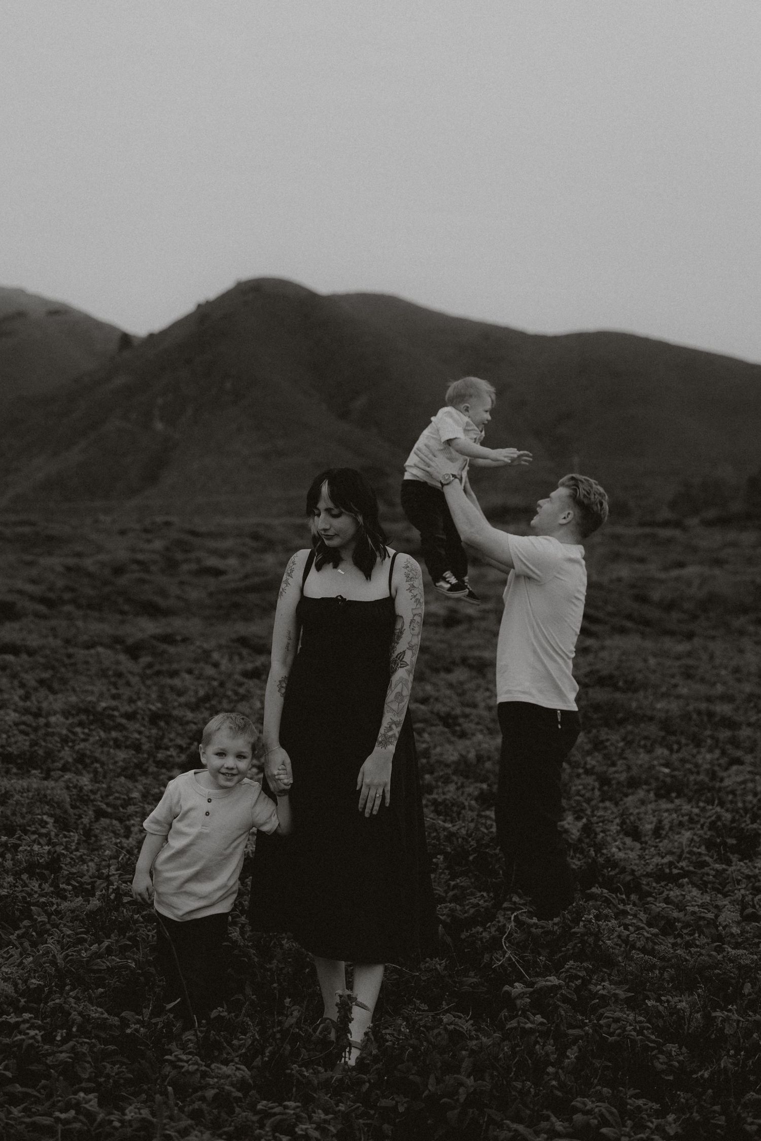 Black and white family photo with parents and two young children in a field with mountains in the background.