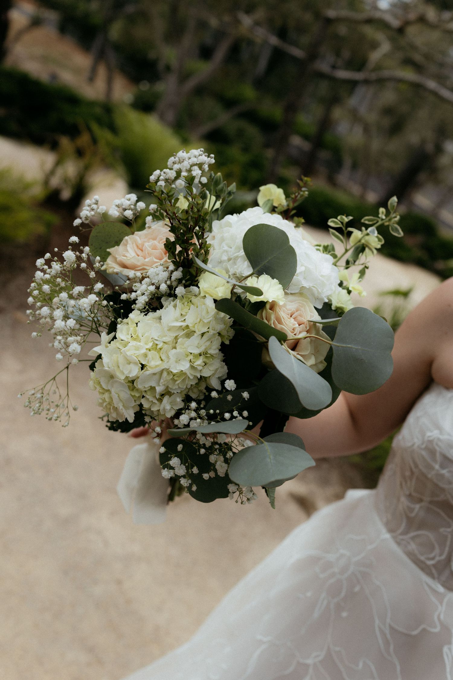 Bride holding elegant wedding bouquet with white hydrangeas, peach roses, baby's breath, and eucalyptus leaves.