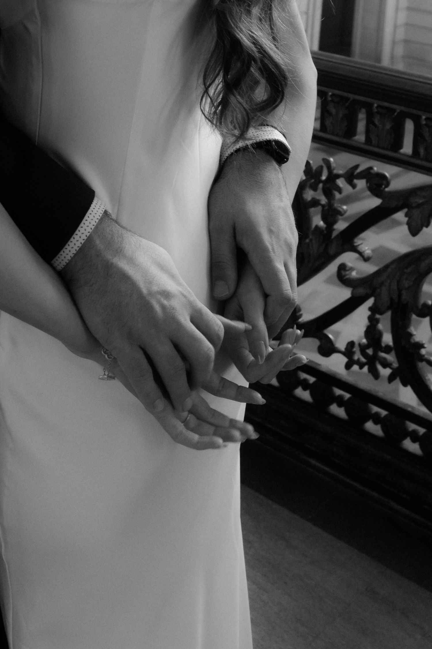 Close-up detail shot of a white wedding dress with hands delicately touching the fabric near ornate railing details.