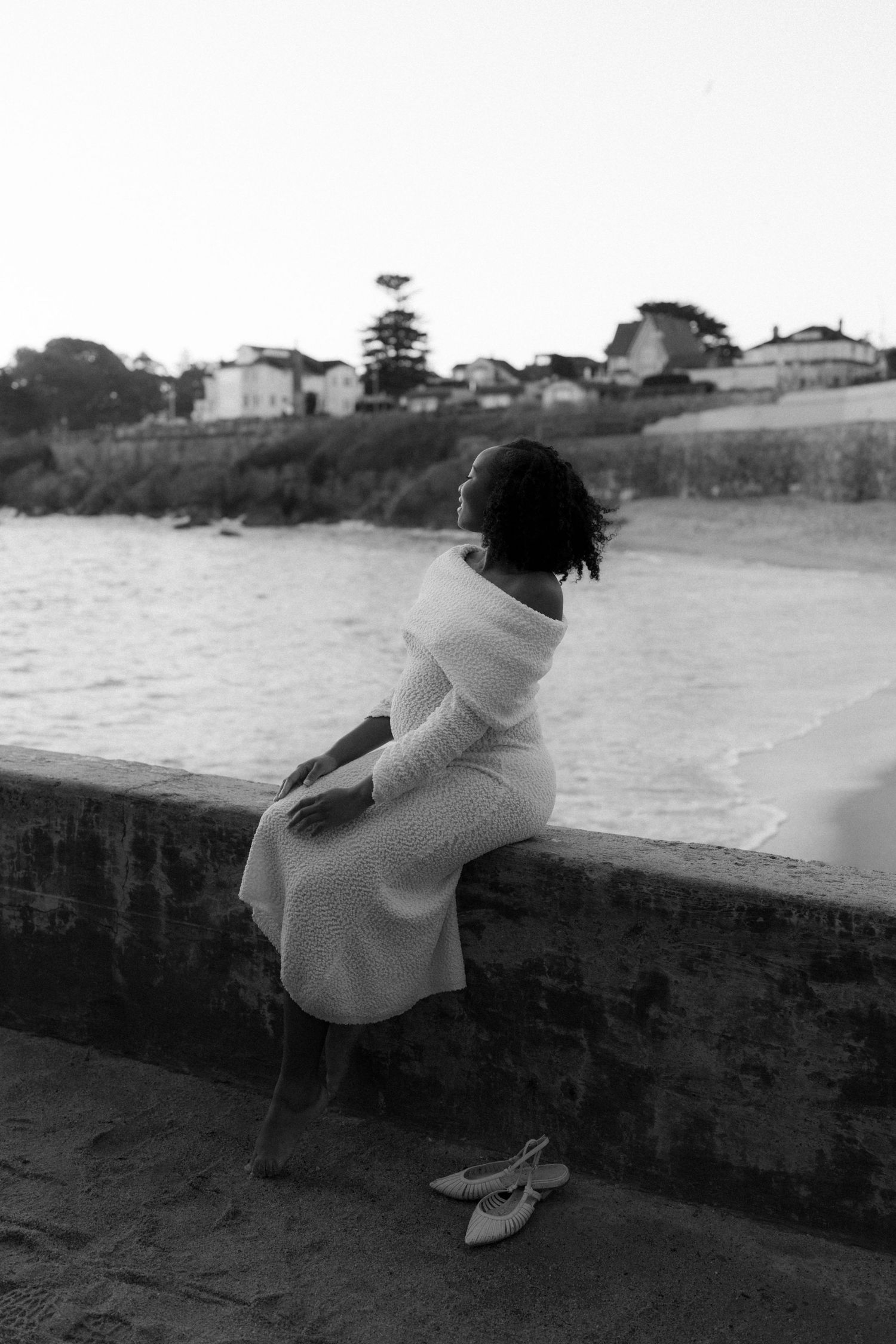 A black and white photo series shows someone sitting on a concrete wall overlooking a scenic coastal view.