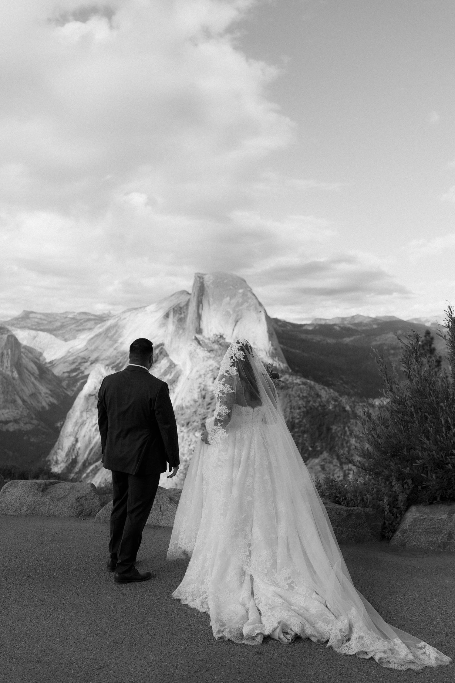 Black and white photo of bride and groom walking toward Half Dome at Yosemite.