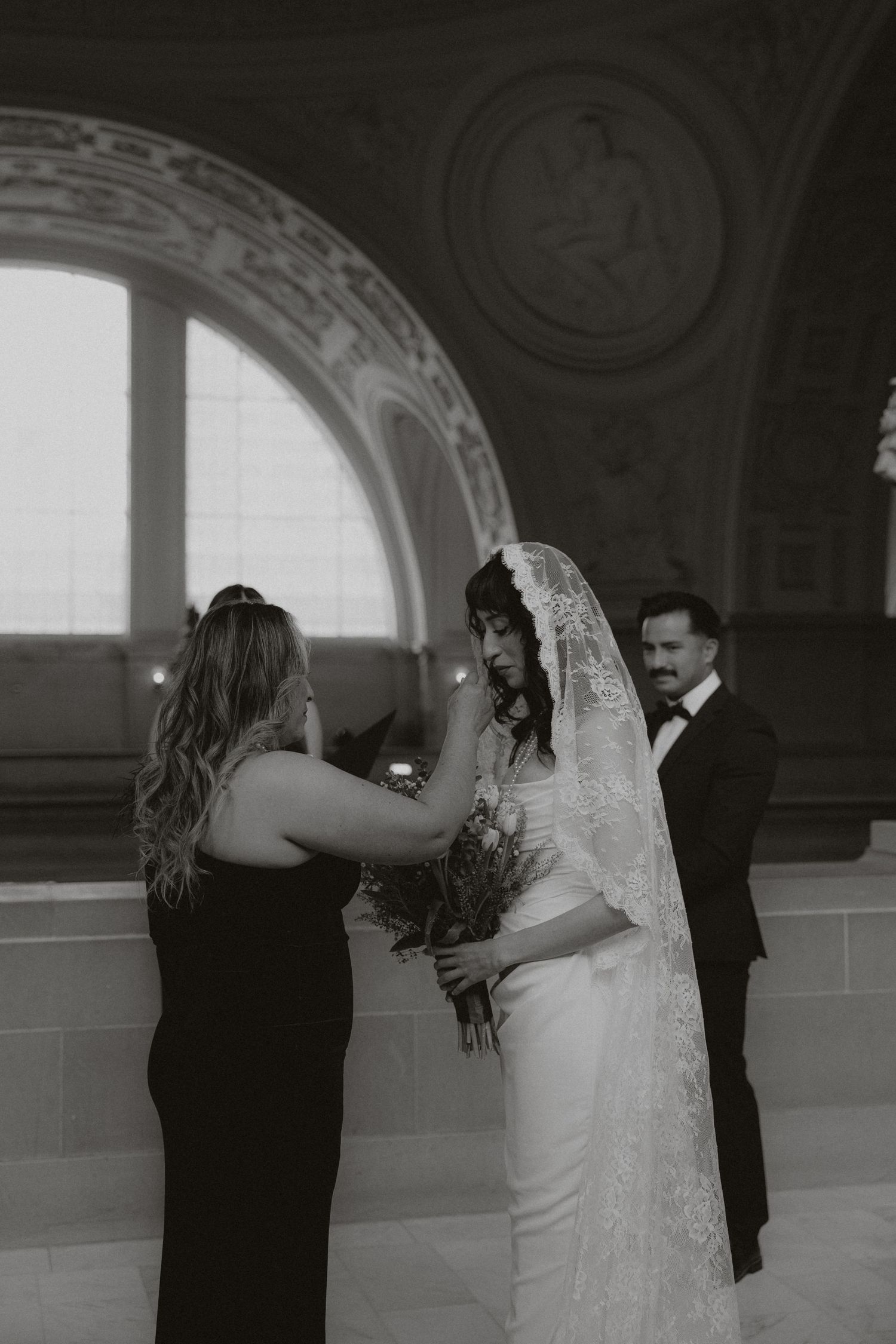 Intimate wedding moment captured in a classical hallway with arched windows and ornate details.