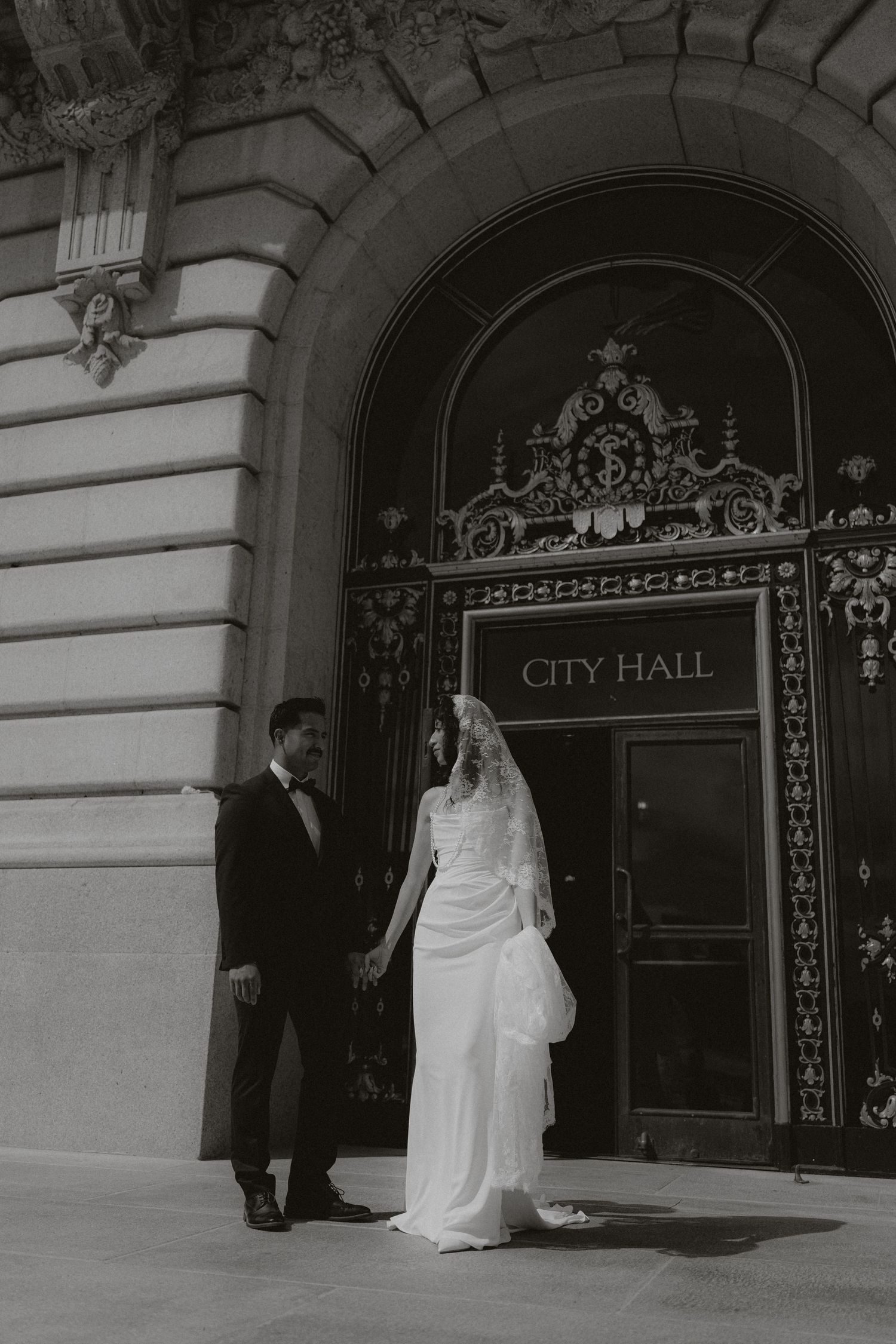 A wedding couple poses elegantly at the entrance of City Hall.
