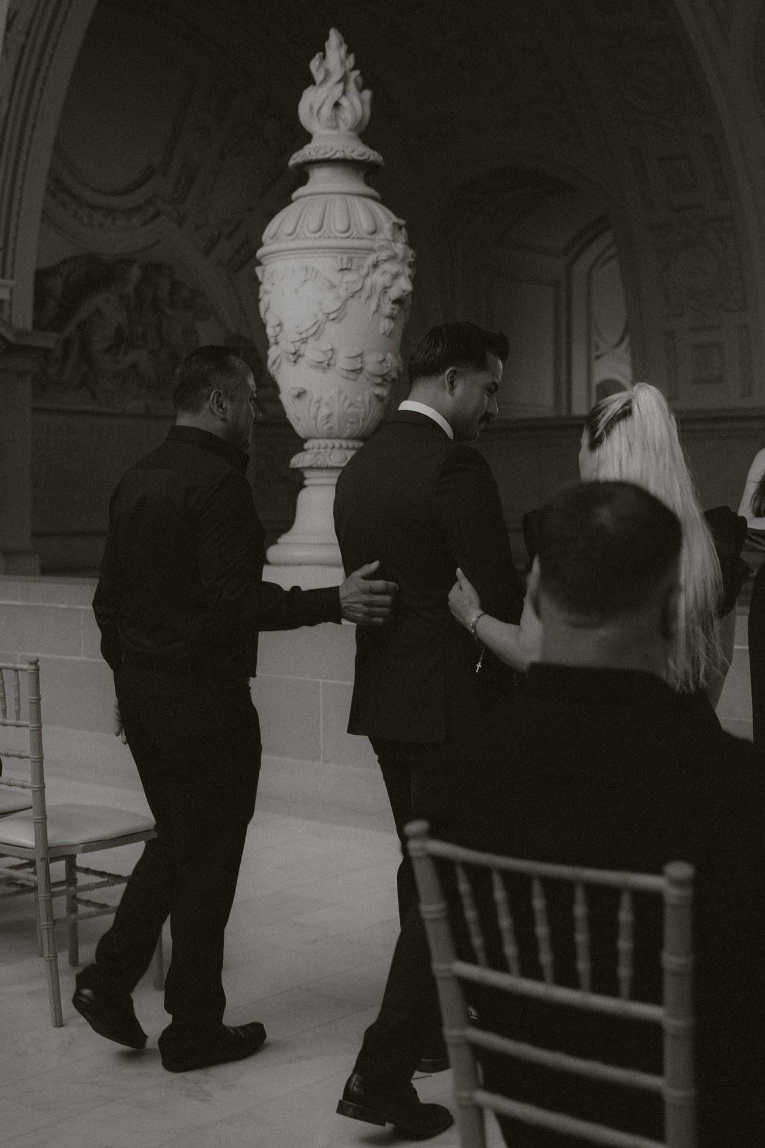 A formal gathering near a decorative white urn in an elegant hall.