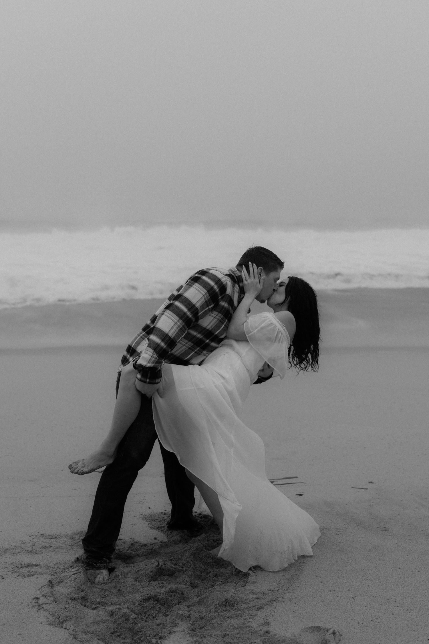 Black and white sequence of a couple playfully falling onto a beach together in wedding attire.