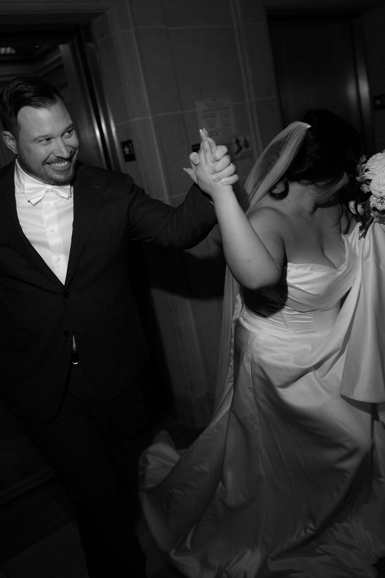 A couple shares a playful moment dancing and laughing together in a dimly lit setting.