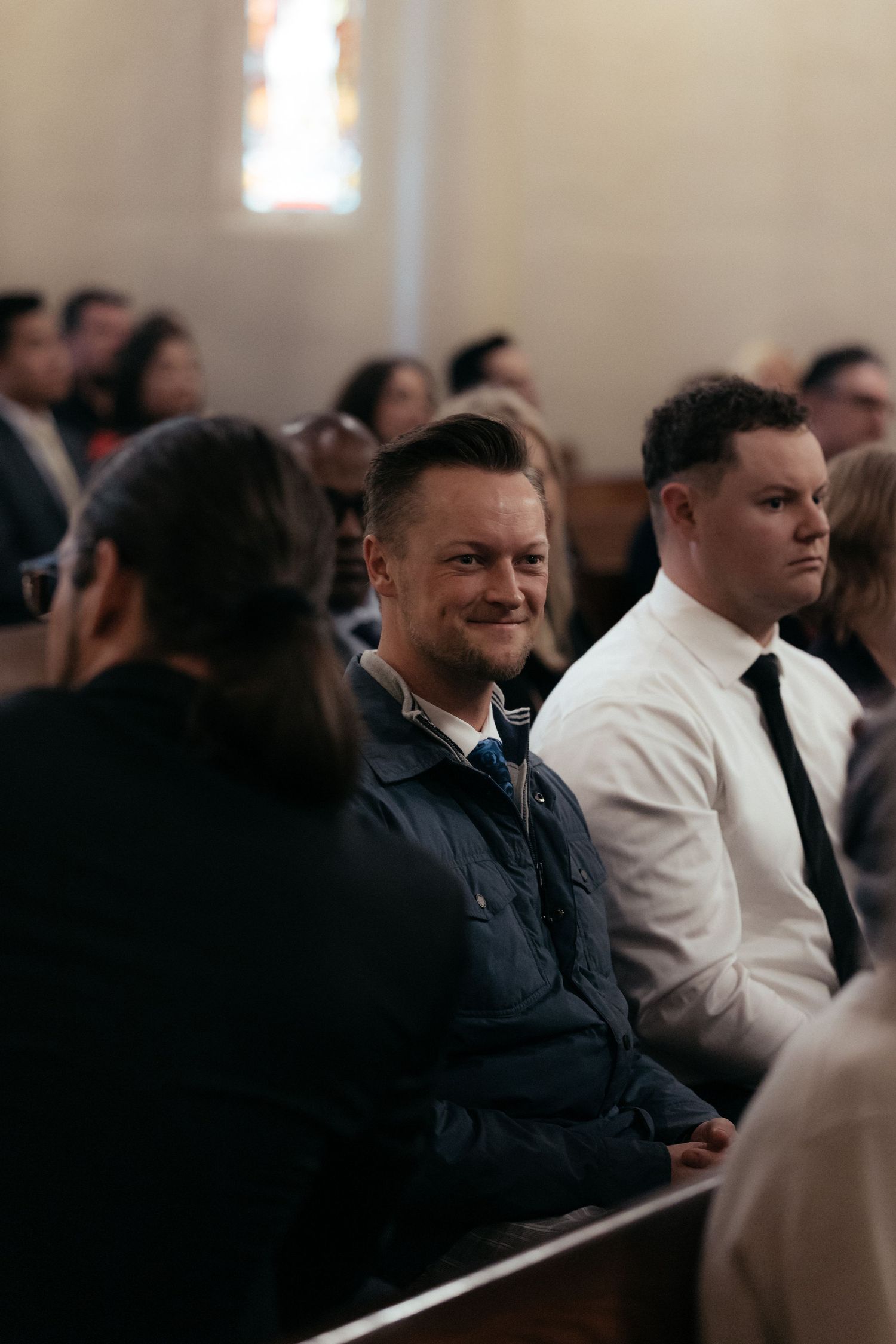 Wedding guests seated in church pews watching the ceremony with joyful expressions.