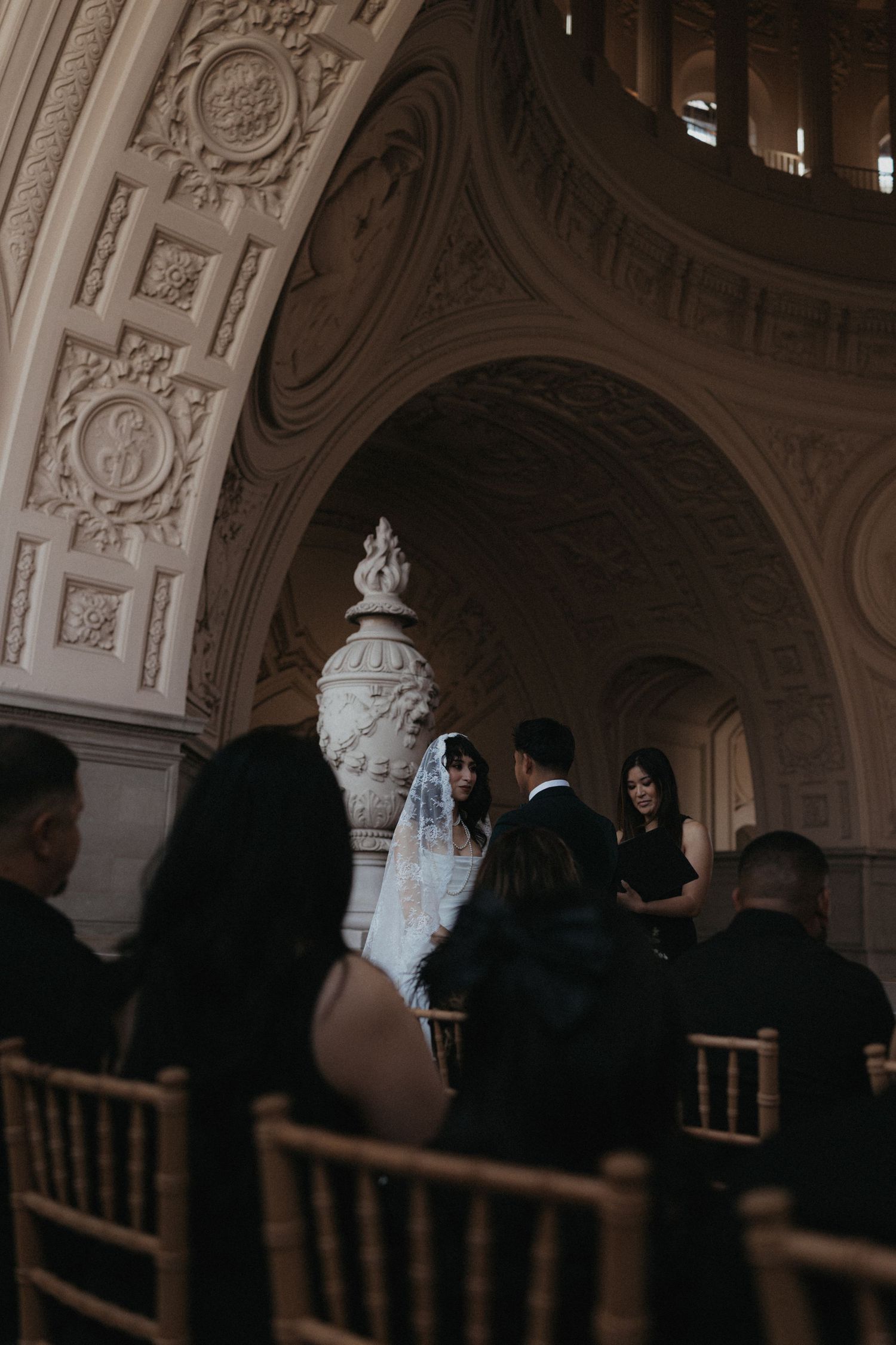 Elegant wedding ceremony under ornate arched ceiling at San Francisco City Hall with bride in lace veil.