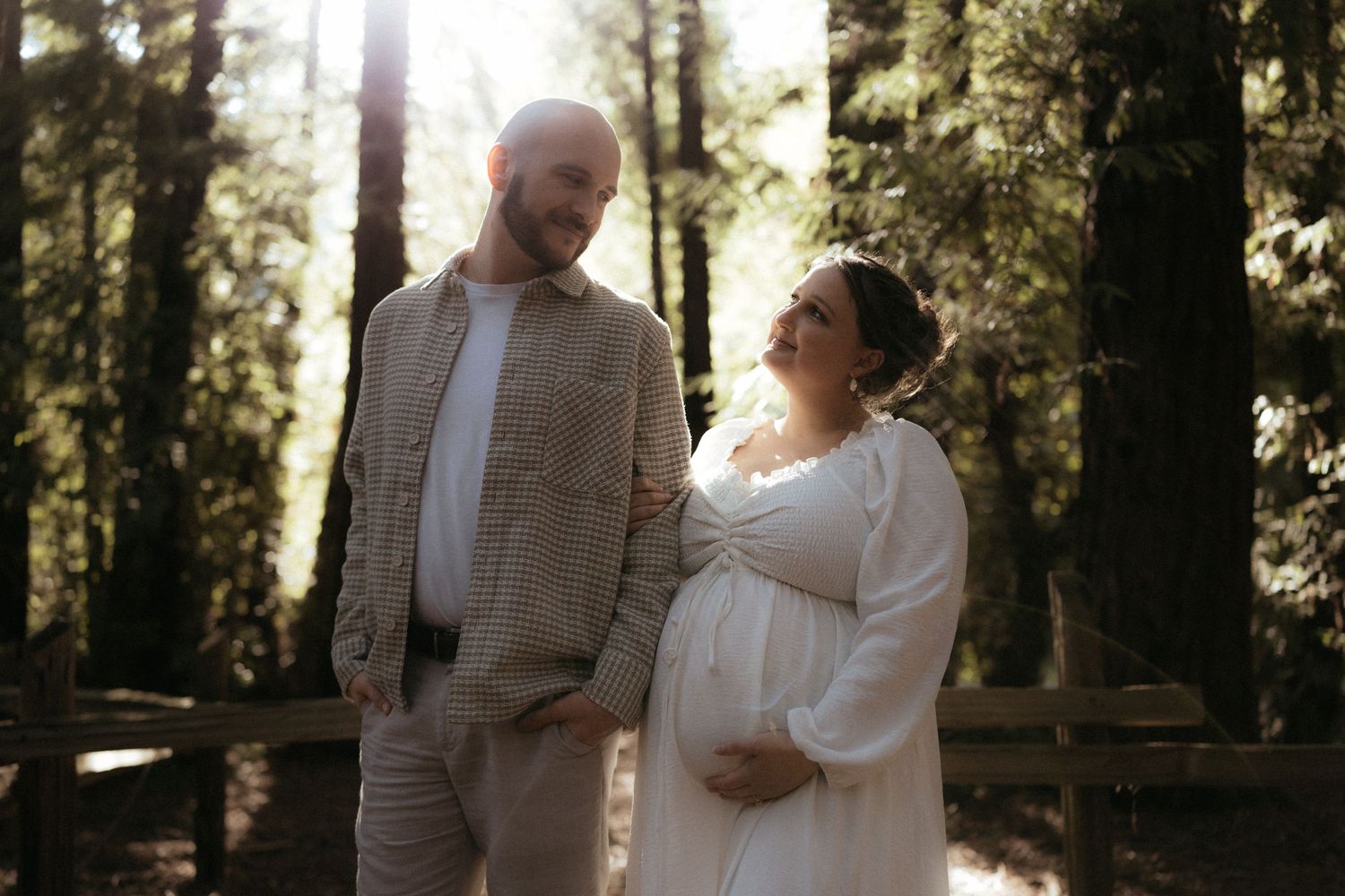 A couple shares a romantic moment in a sunlit forest setting during their wedding celebration.