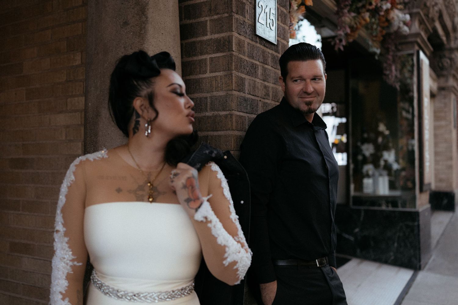 Wedding couple poses outside brick building with elegant floral decorations.