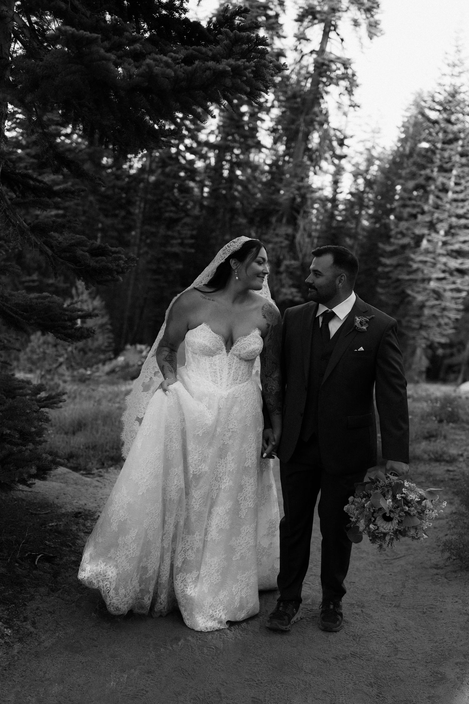 Bride and groom walking hand in hand through forest in black and white wedding photo.
