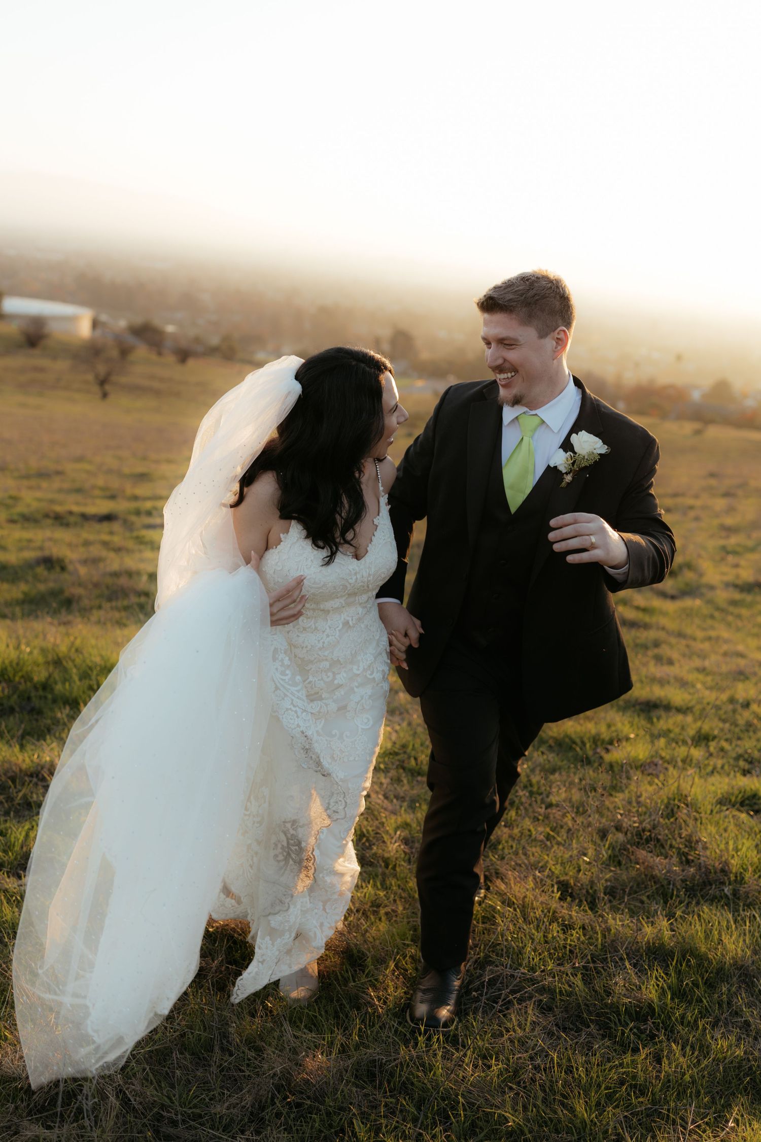 A newlywed couple playfully poses in a misty field during golden hour sunset for their wedding photos.