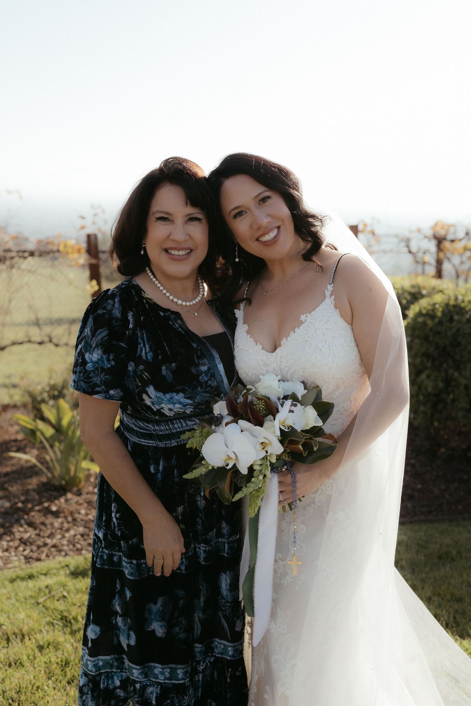 Bridal party members share joyful moments together outdoors during a vineyard wedding celebration.