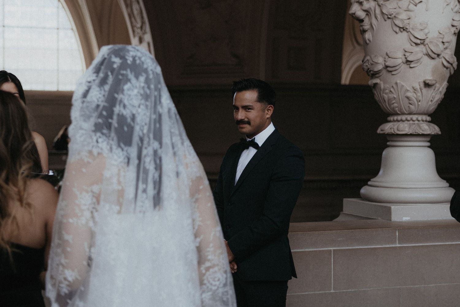 Wedding party members walking through a grand corridor with decorative moldings and arches.