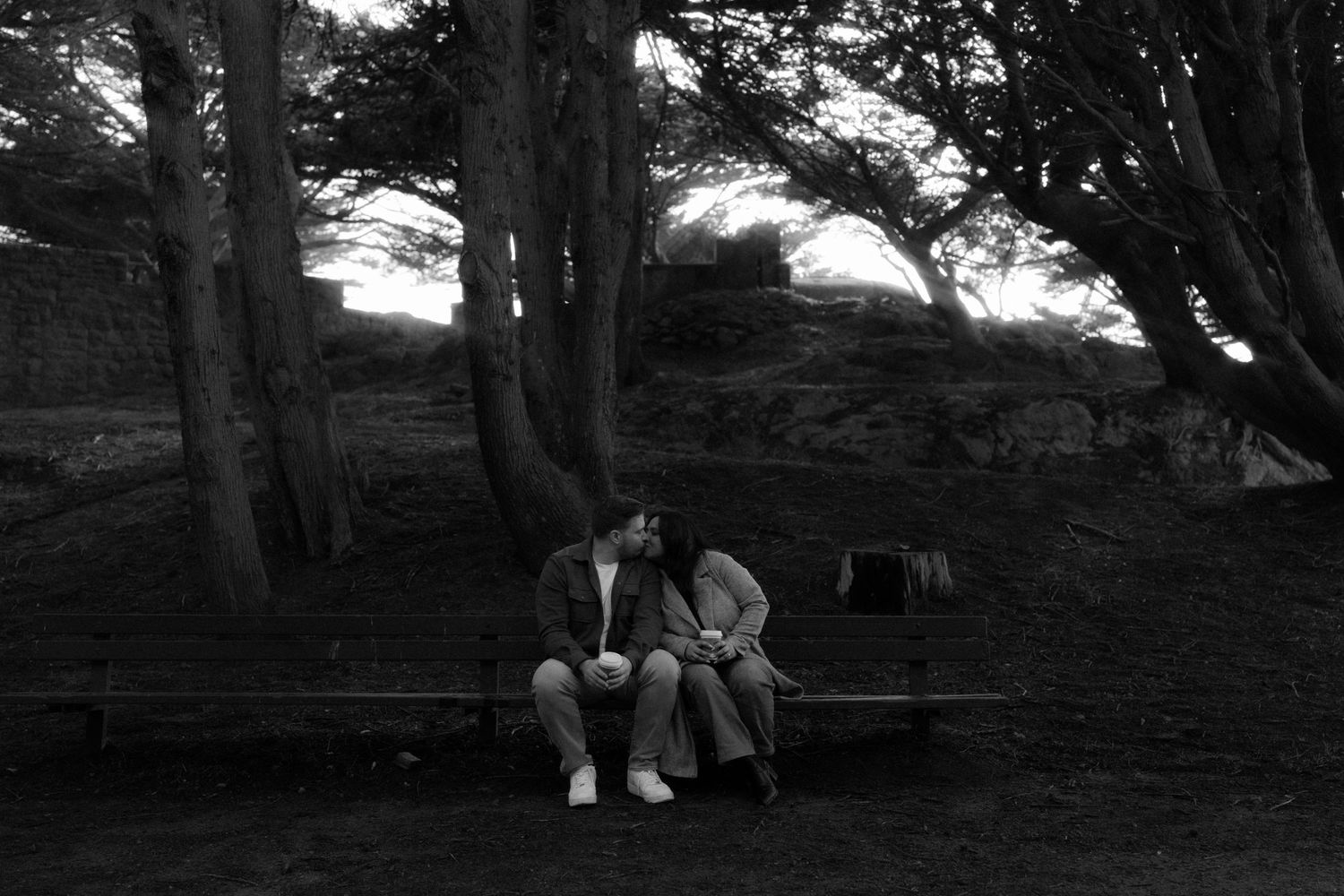 A romantic wedding photoshoot under tall cypress trees in a misty forest setting.