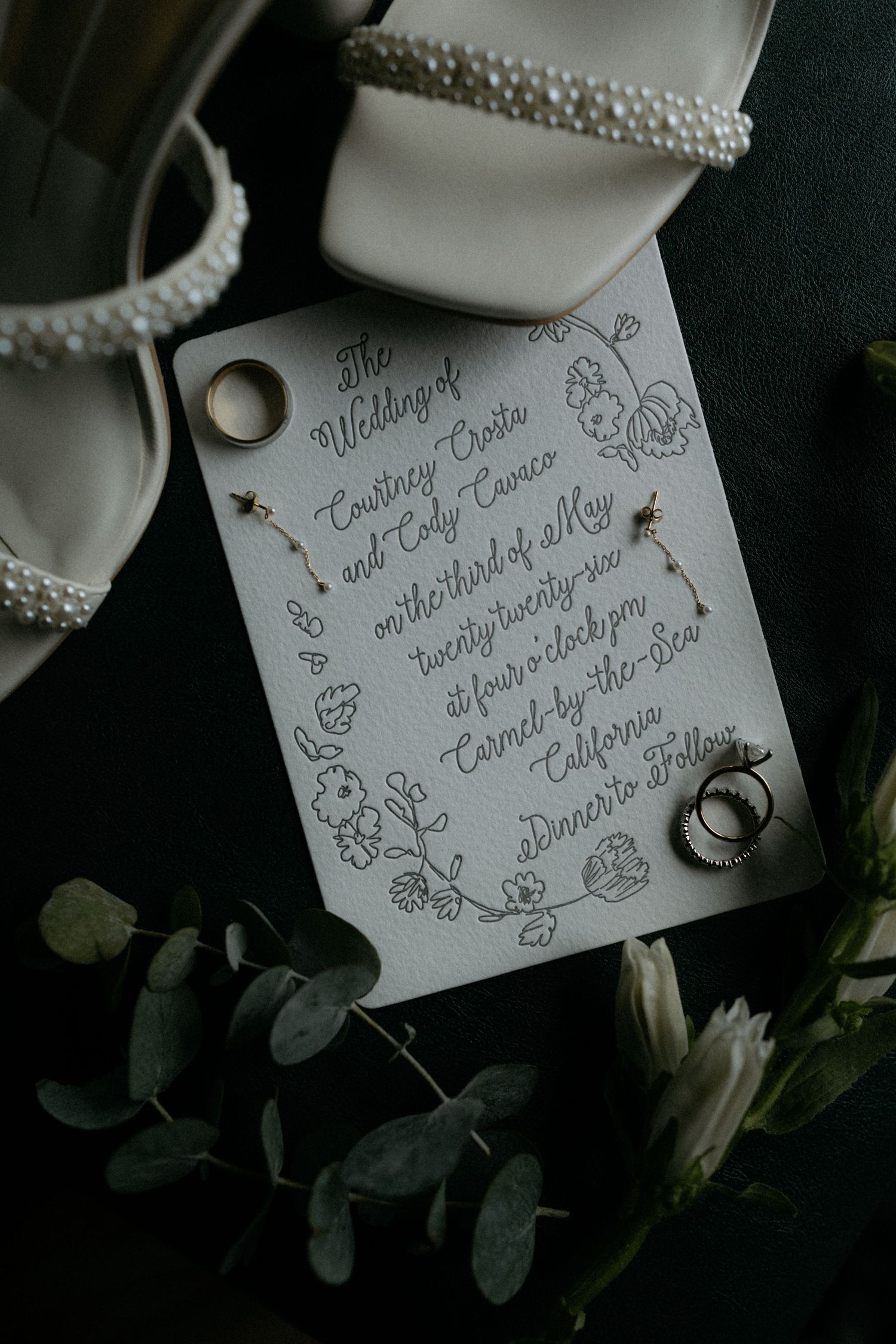 Elegant wedding invitation for Courtney Costa and Cody Cameo surrounded by pearl heels, rings, and eucalyptus.