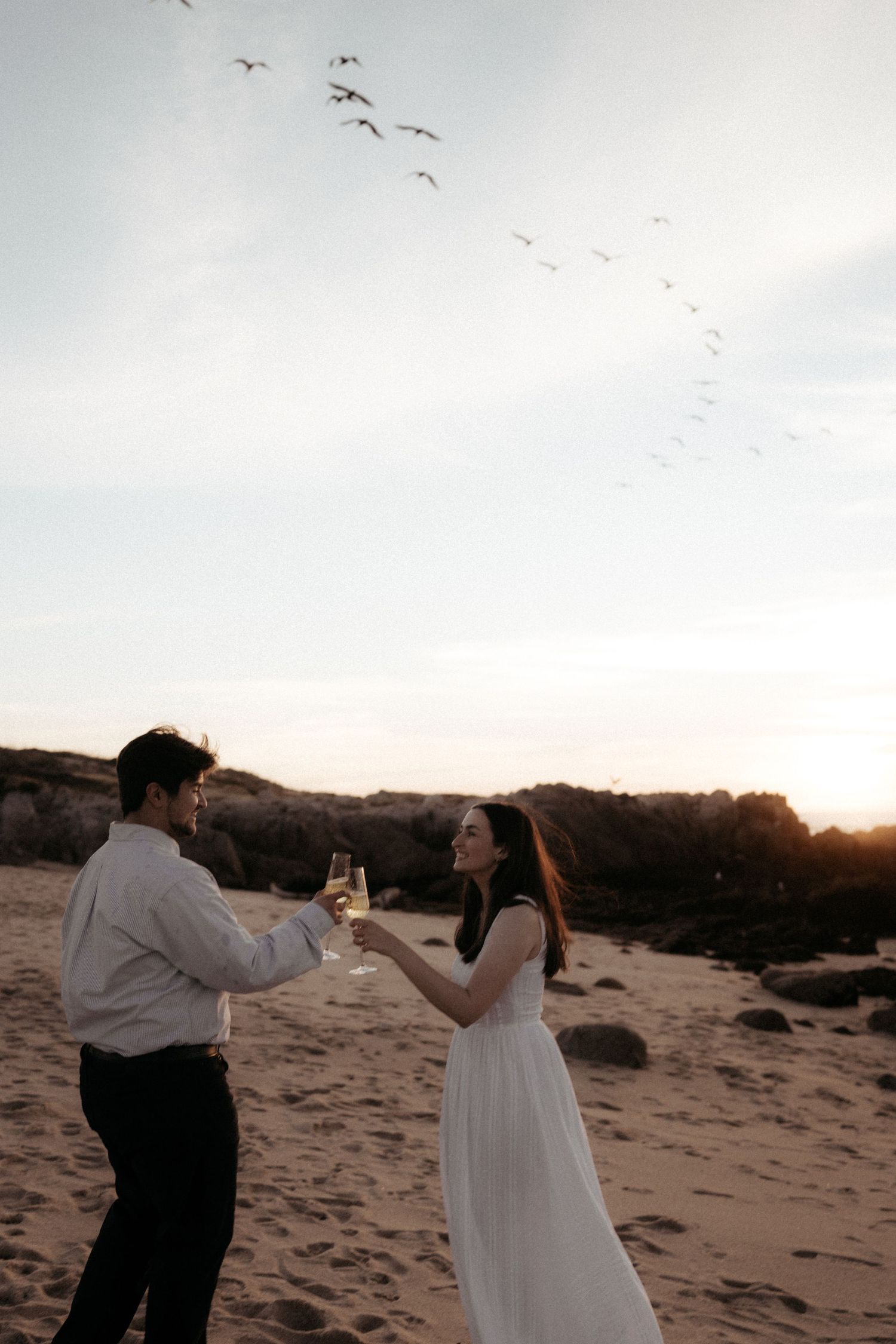 Silhouetted figures dance on a beach with seabirds flying overhead during a dreamy sunset photoshoot.