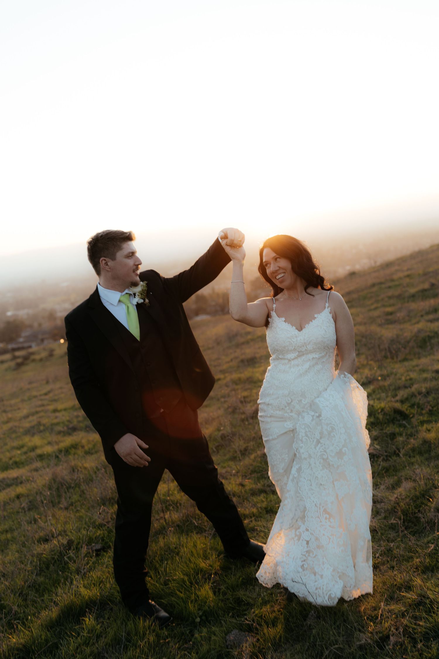 Newlyweds dance together on a hilltop during golden hour.