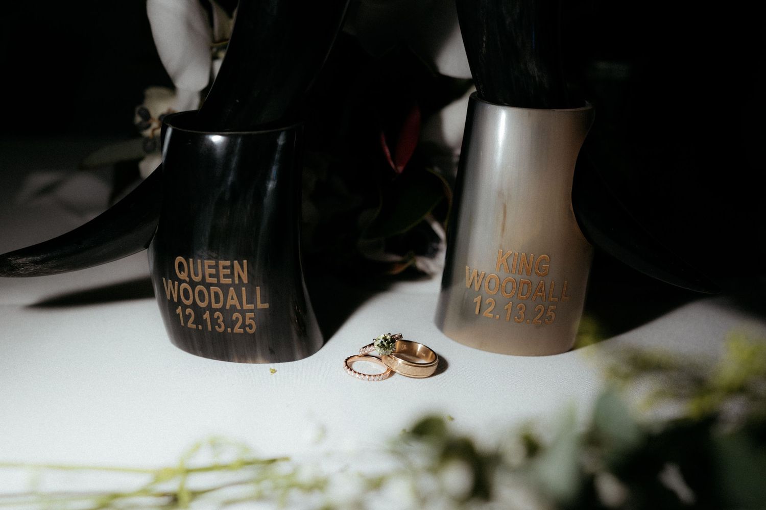 Wedding rings rest on a textured white surface with bottles and decor in the background.