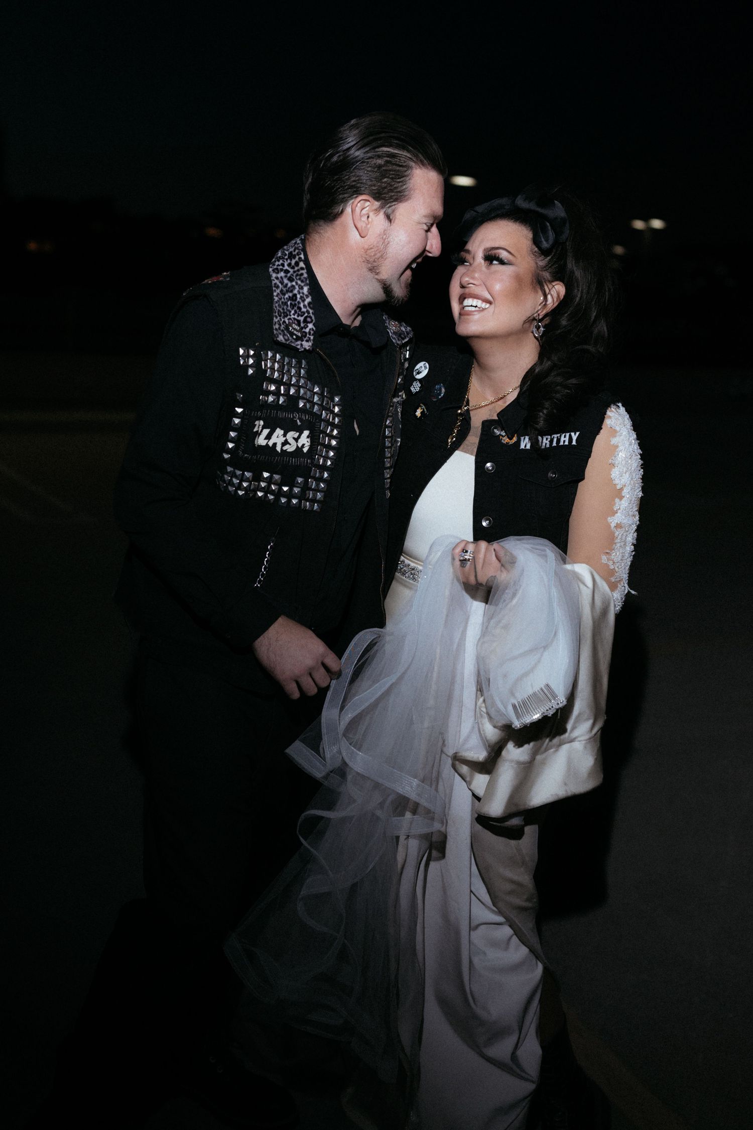 A romantic couple in contrasting punk and wedding attire share an intimate moment in low light.