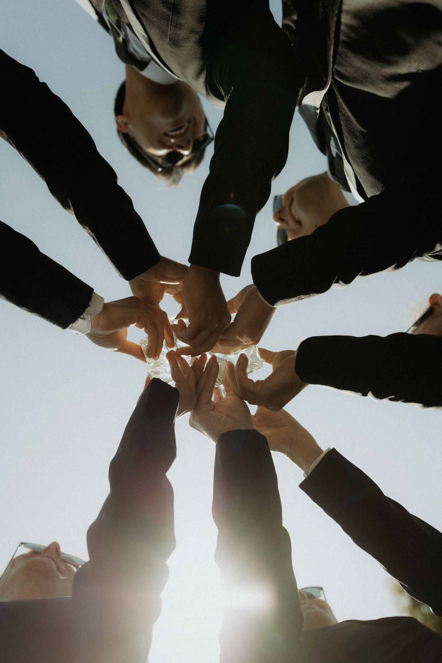Business team joining hands together in a circle formation against bright sunlight, symbolizing unity and teamwork.