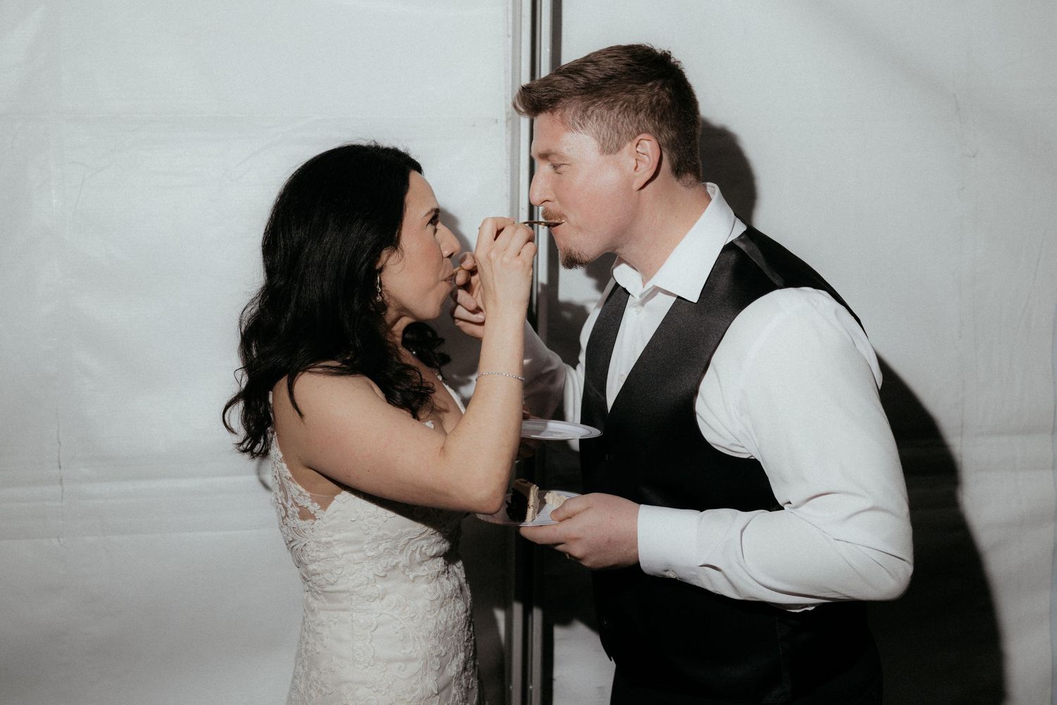 A couple in wedding attire share a playful moment while singing into a microphone at their reception.