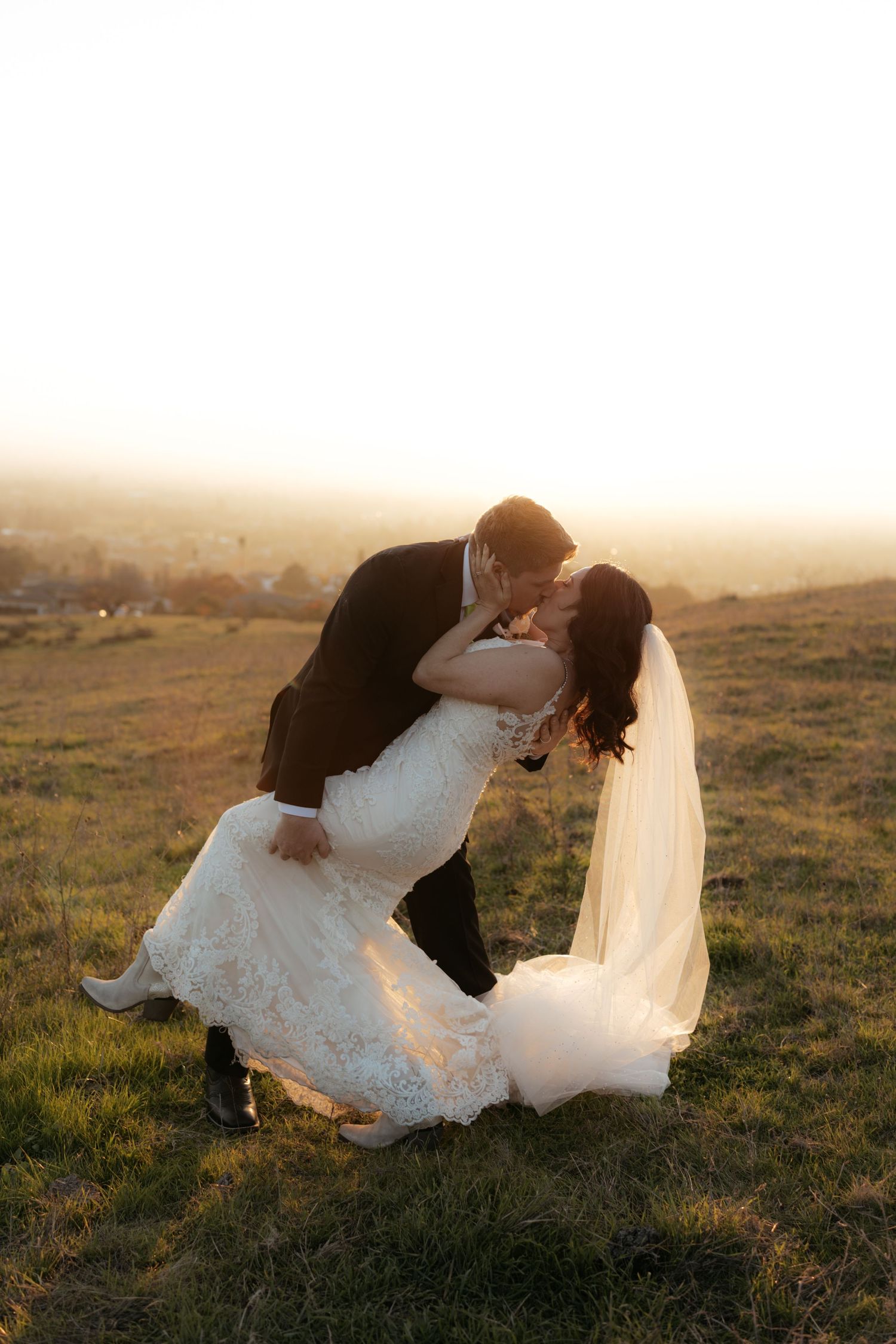 A romantic wedding couple shares an intimate dip pose in a sunlit field at golden hour.