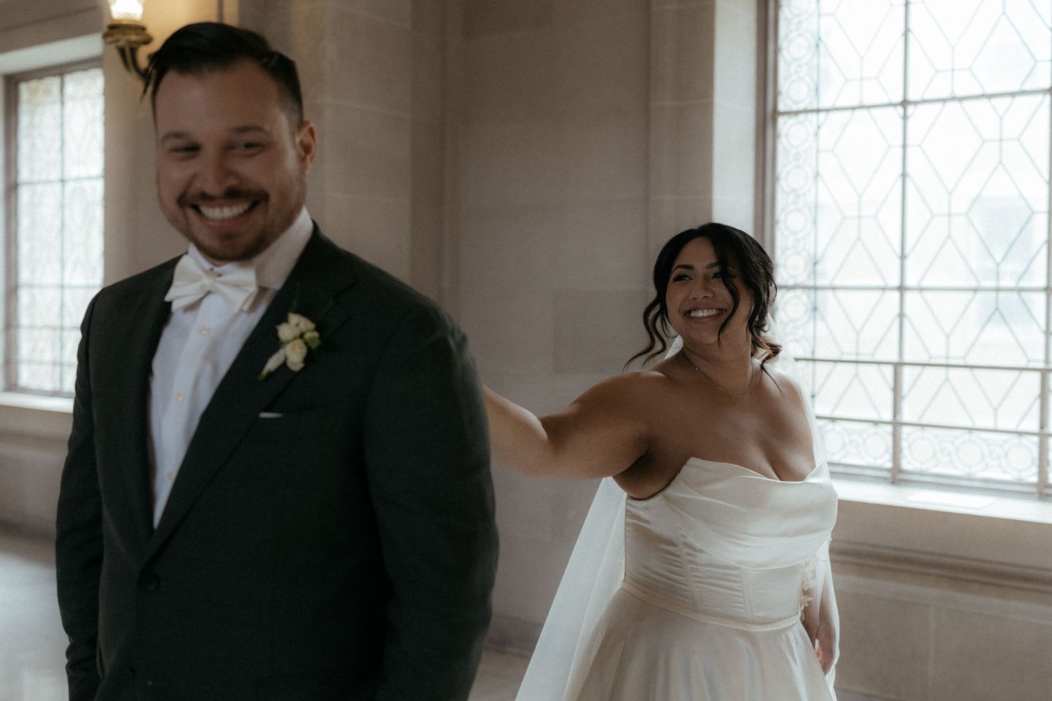 A wedding couple shares joyful moments together in a bright indoor setting with white decor and natural lighting.